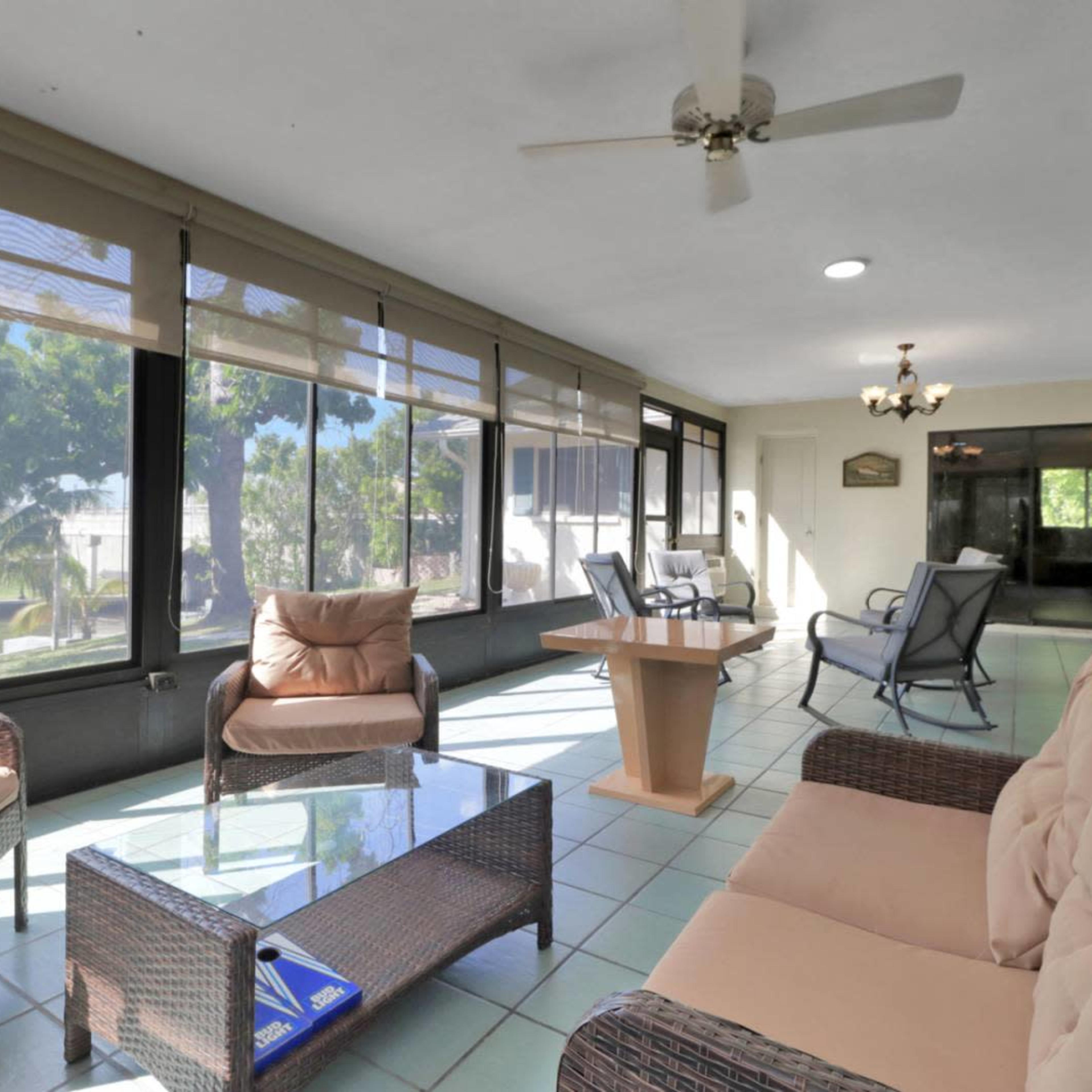 A sunroom furnished with a glass-top table, comfortable seating, and large windows allowing natural light to enter.