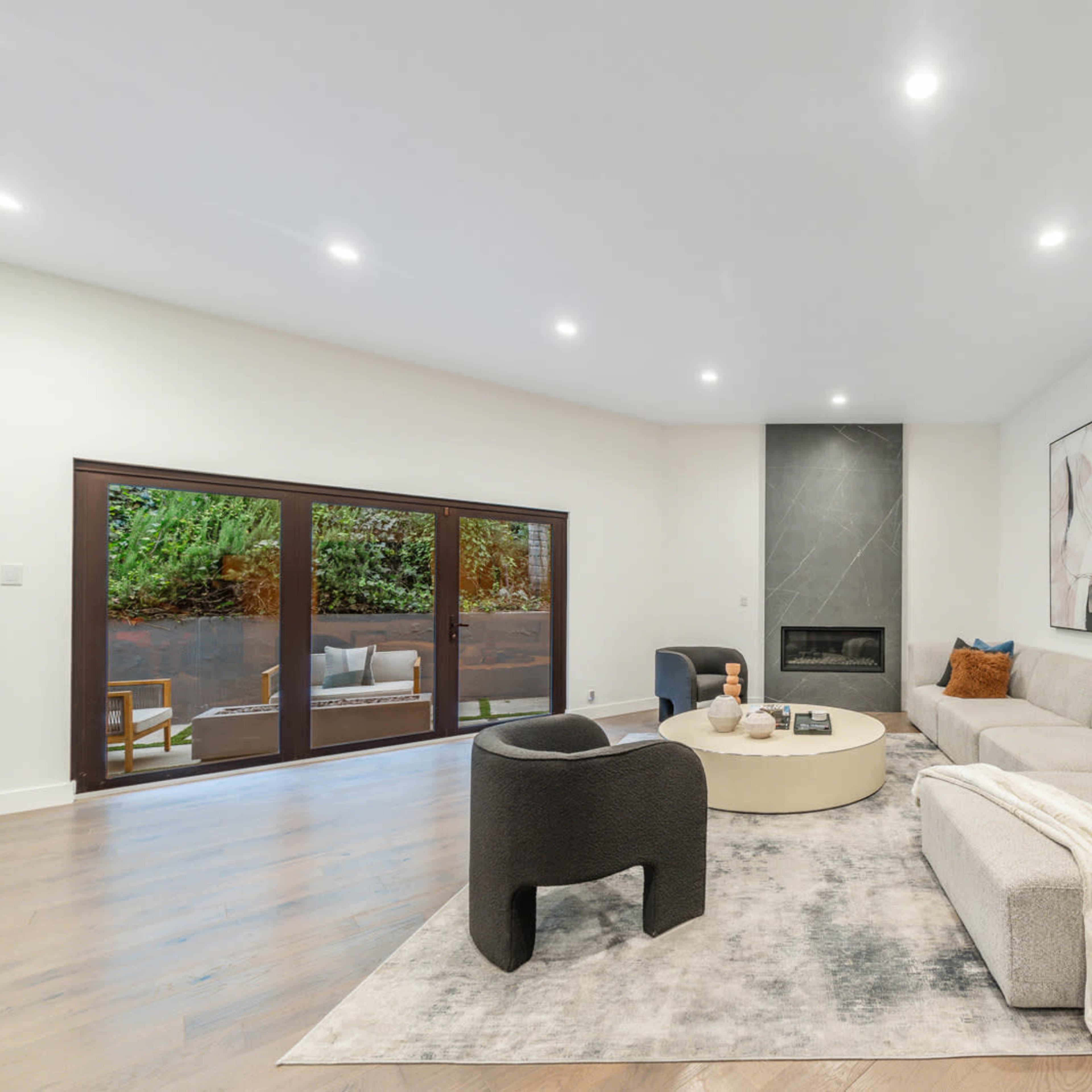 A modern living room with a light gray sofa, a round coffee table, and large windows overlooking a patio area.