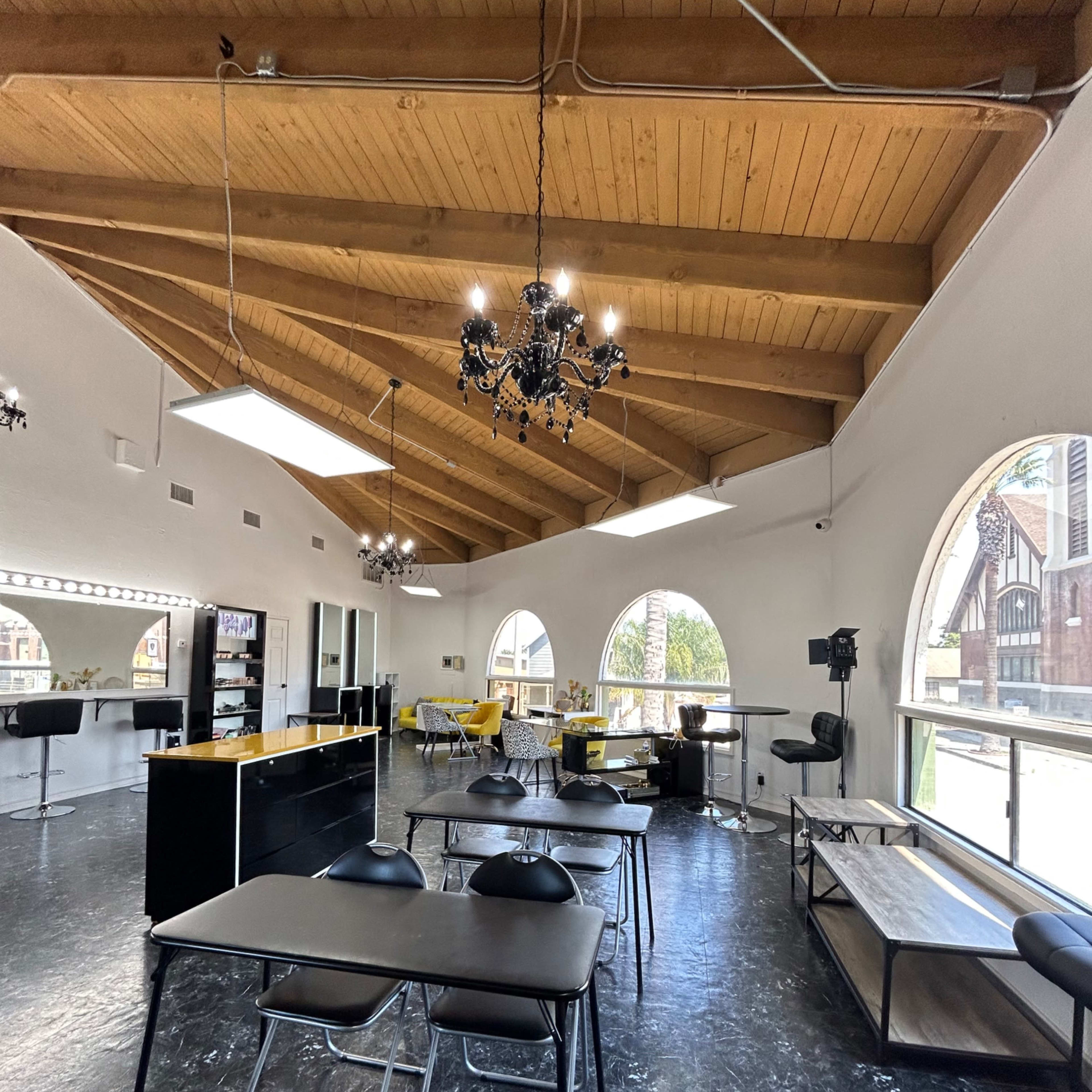 A spacious salon interior with wooden beams, large windows, and several black tables and chairs.