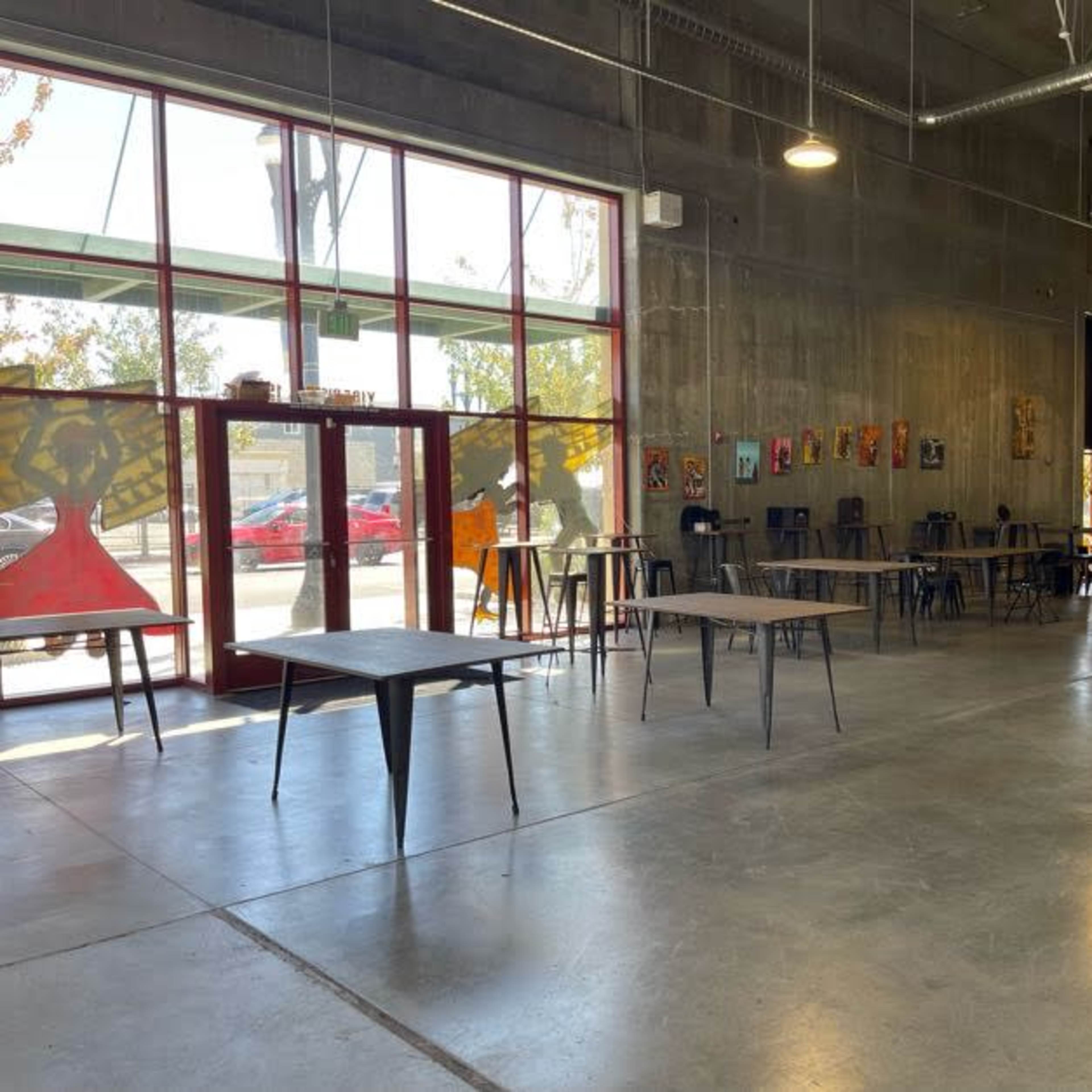 A spacious interior of a modern venue with high ceilings, large windows, and tables set up in an industrial-style room.