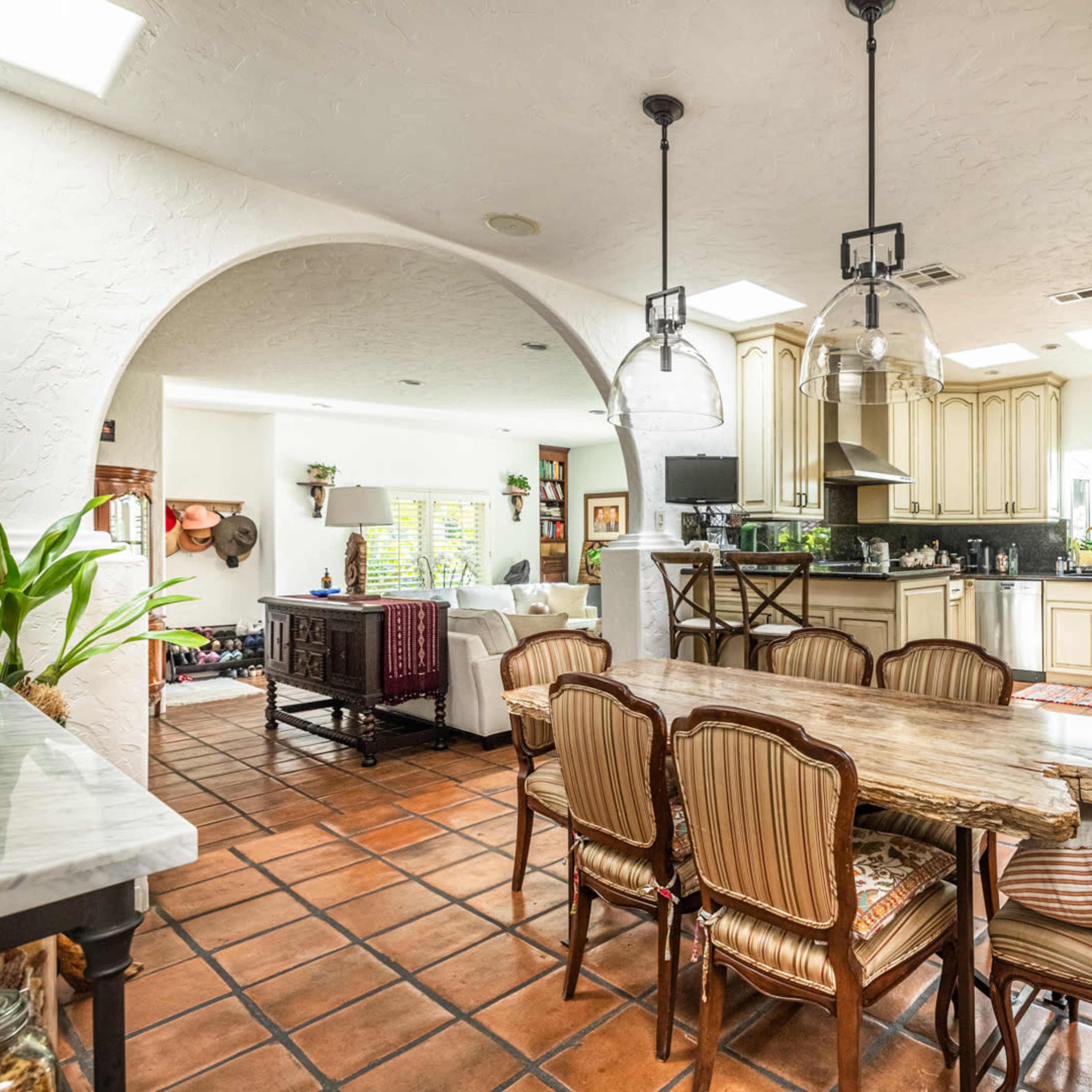 A spacious kitchen and dining area features a large wooden table surrounded by chairs, connected to a well-equipped kitchen through an archway.