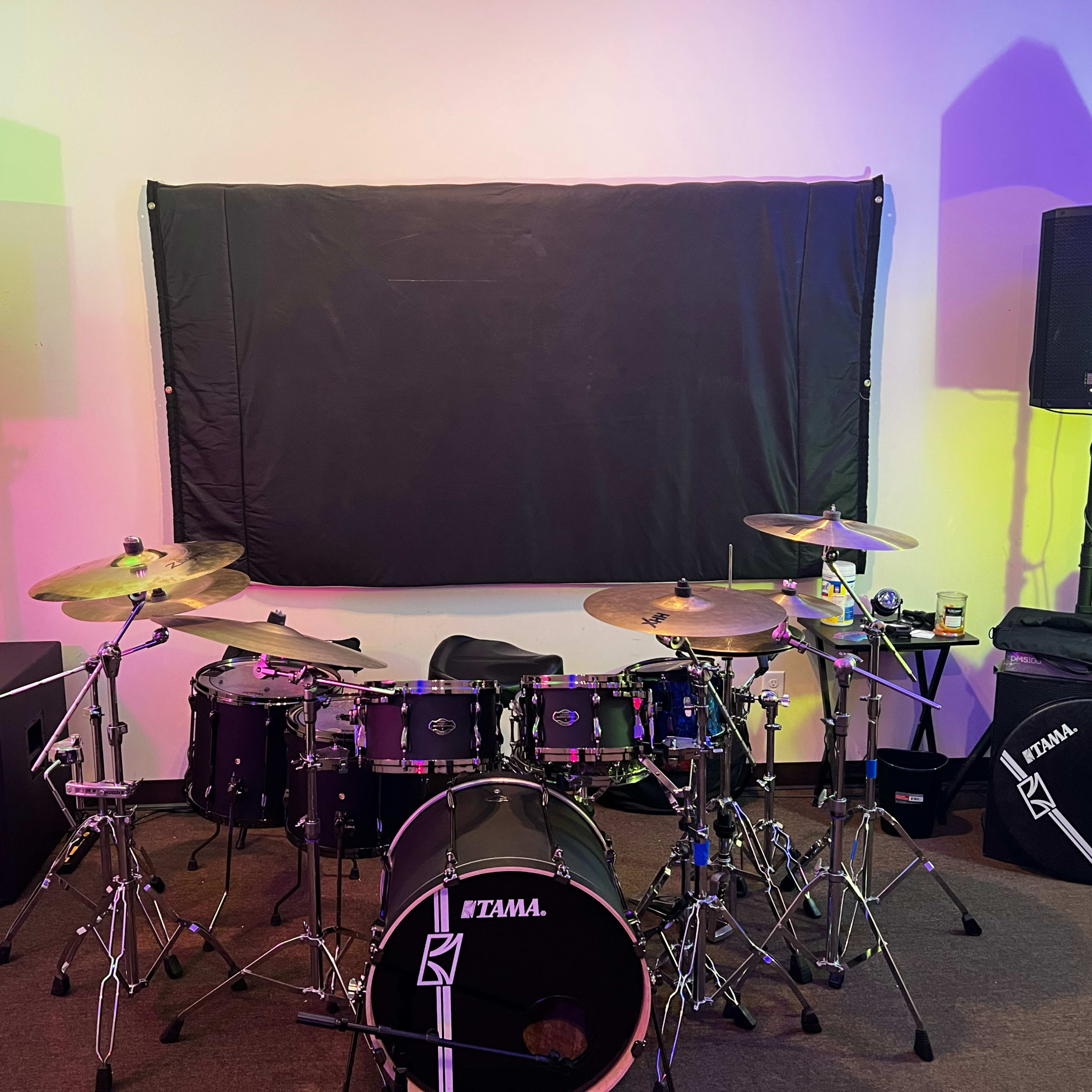 A drum kit with cymbals set up in a music studio, flanked by large speakers on either side.