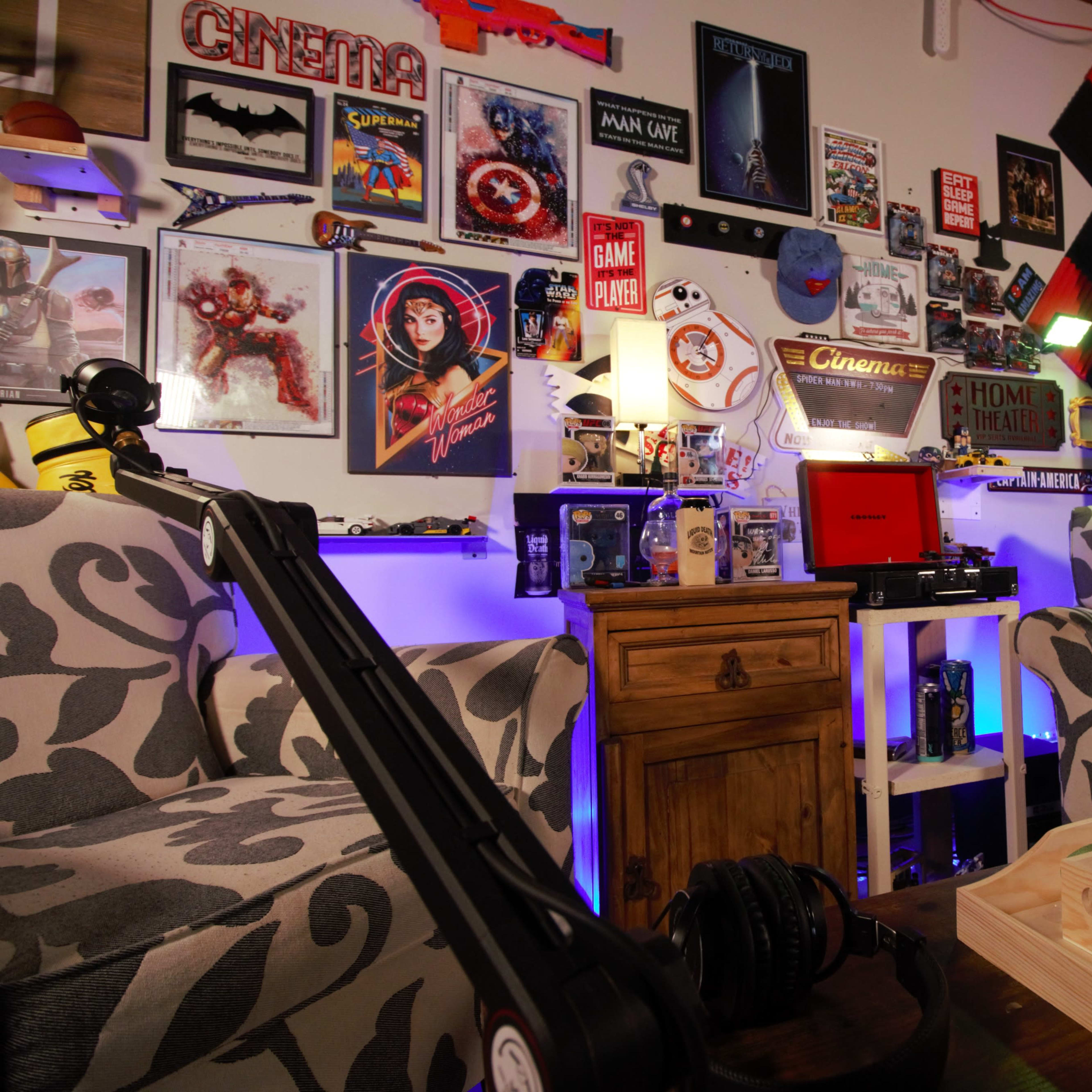 A cozy entertainment corner featuring two patterned armchairs, a wooden side table, a vintage record player, and a wall adorned with various movie posters and collectibles.