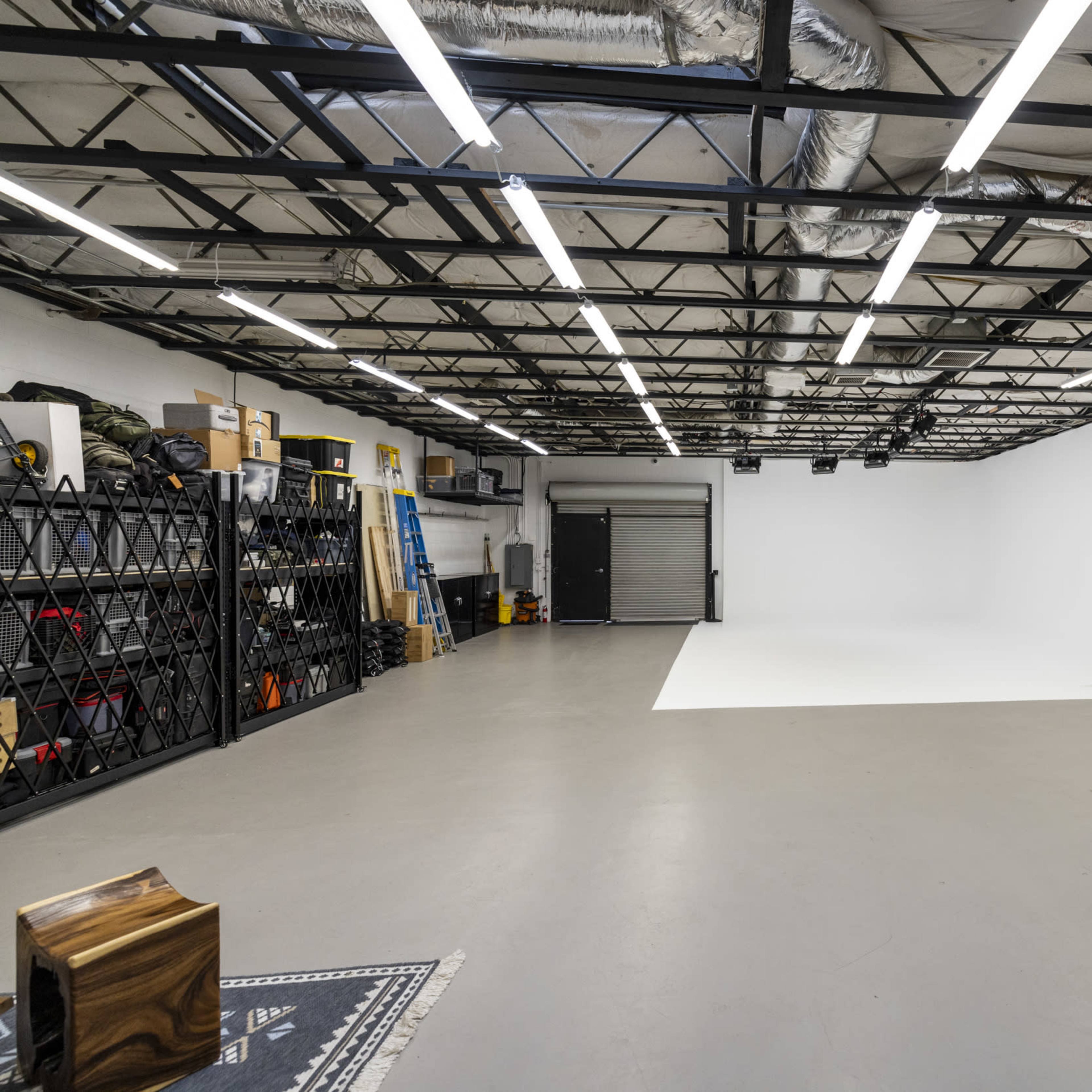 A spacious, brightly lit studio with a white backdrop, storage shelves, and various equipment neatly organized along the walls.