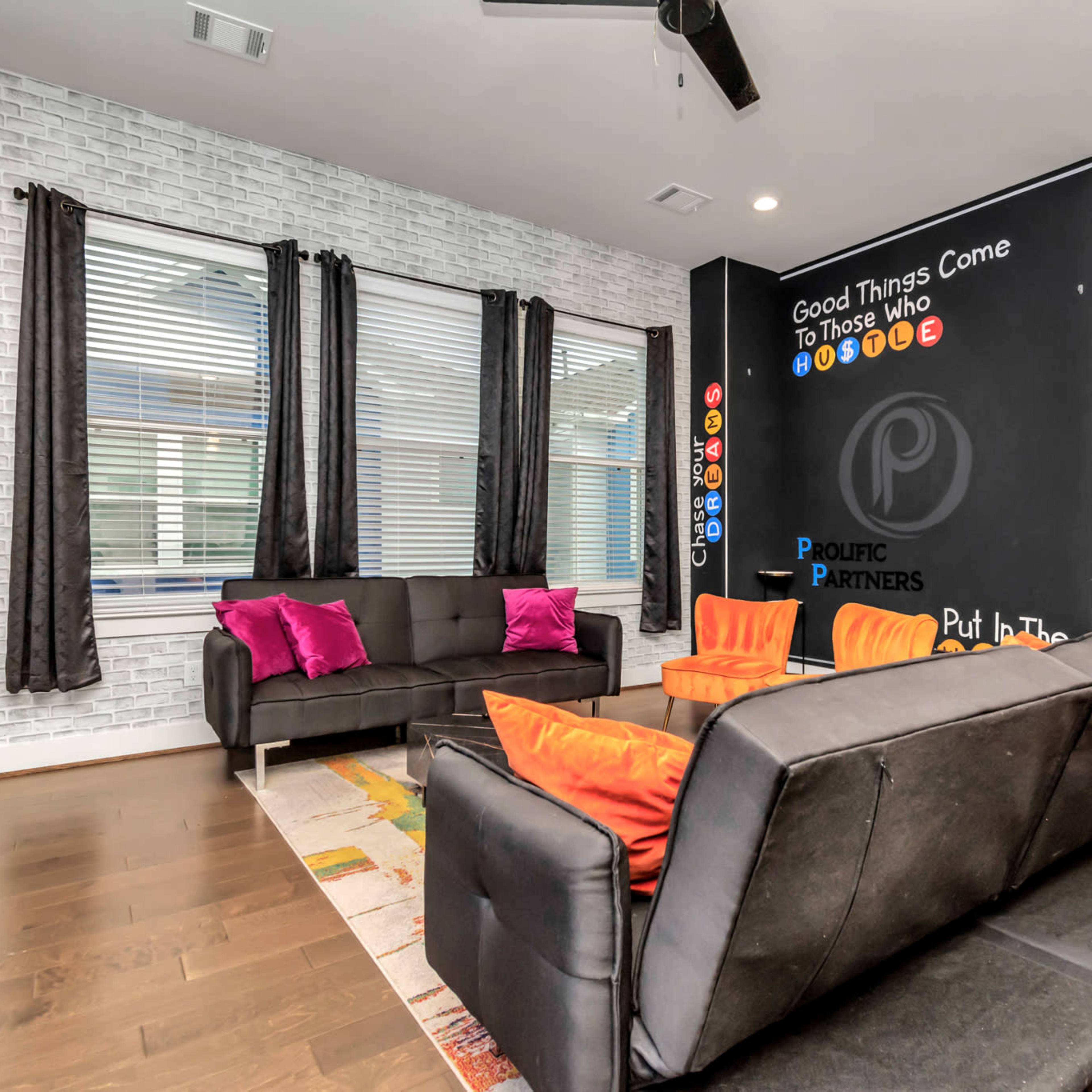 The room features a modern seating area with a black sofa, colorful chairs, and a chalkboard wall with motivational text.