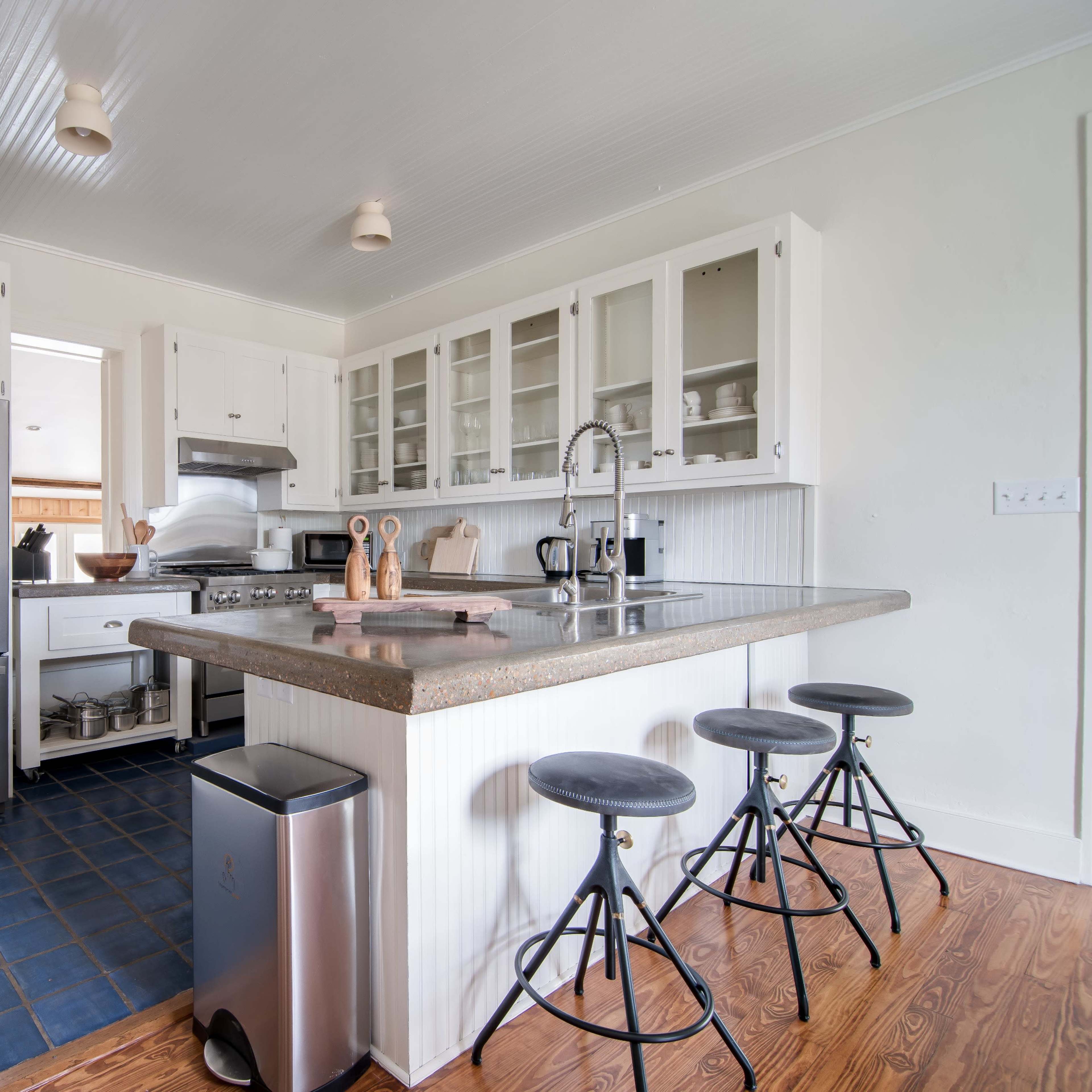 A modern kitchen features a central island with three stools, stainless steel appliances, and white cabinetry.