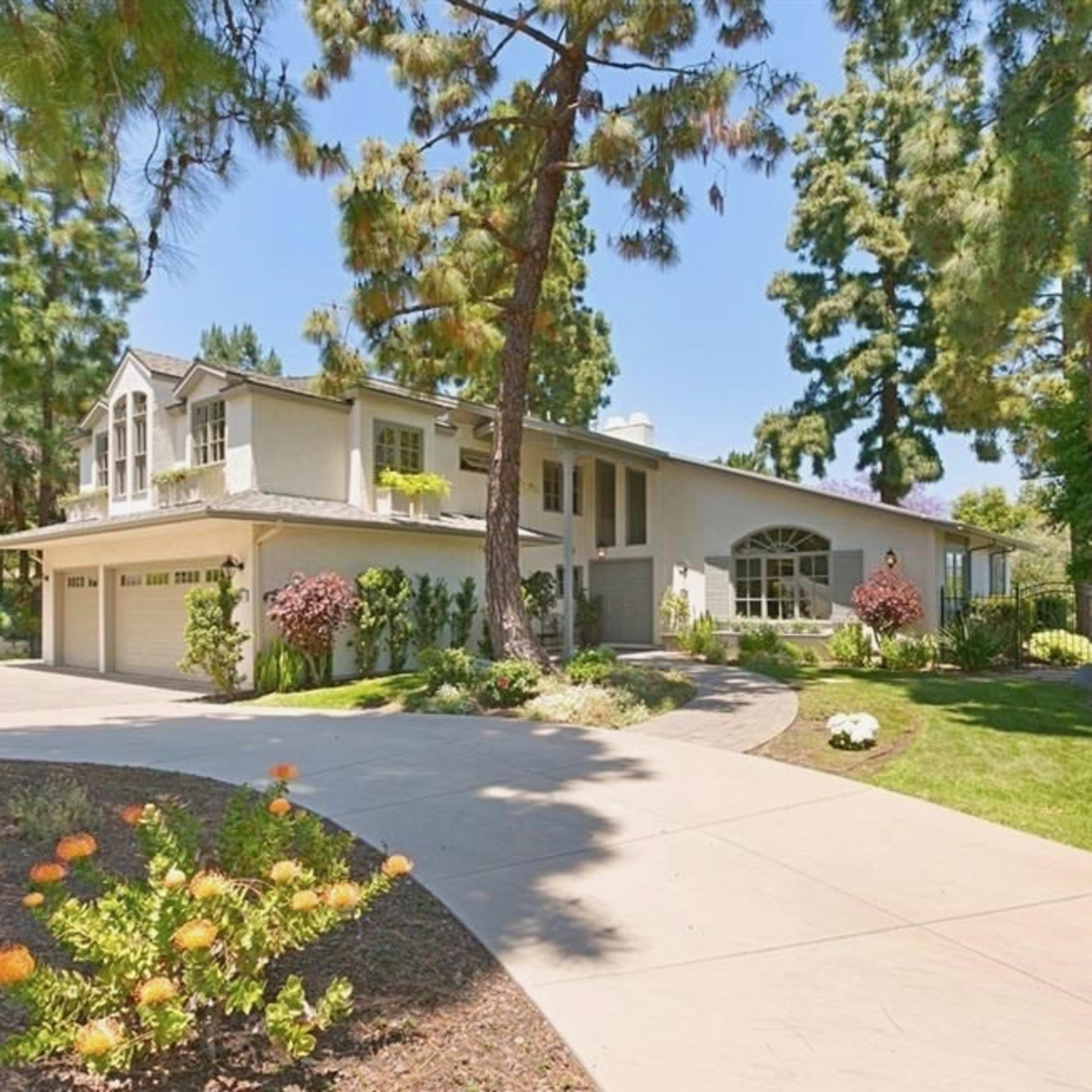 A two-story house with a curved driveway is surrounded by trees and landscaped gardens.