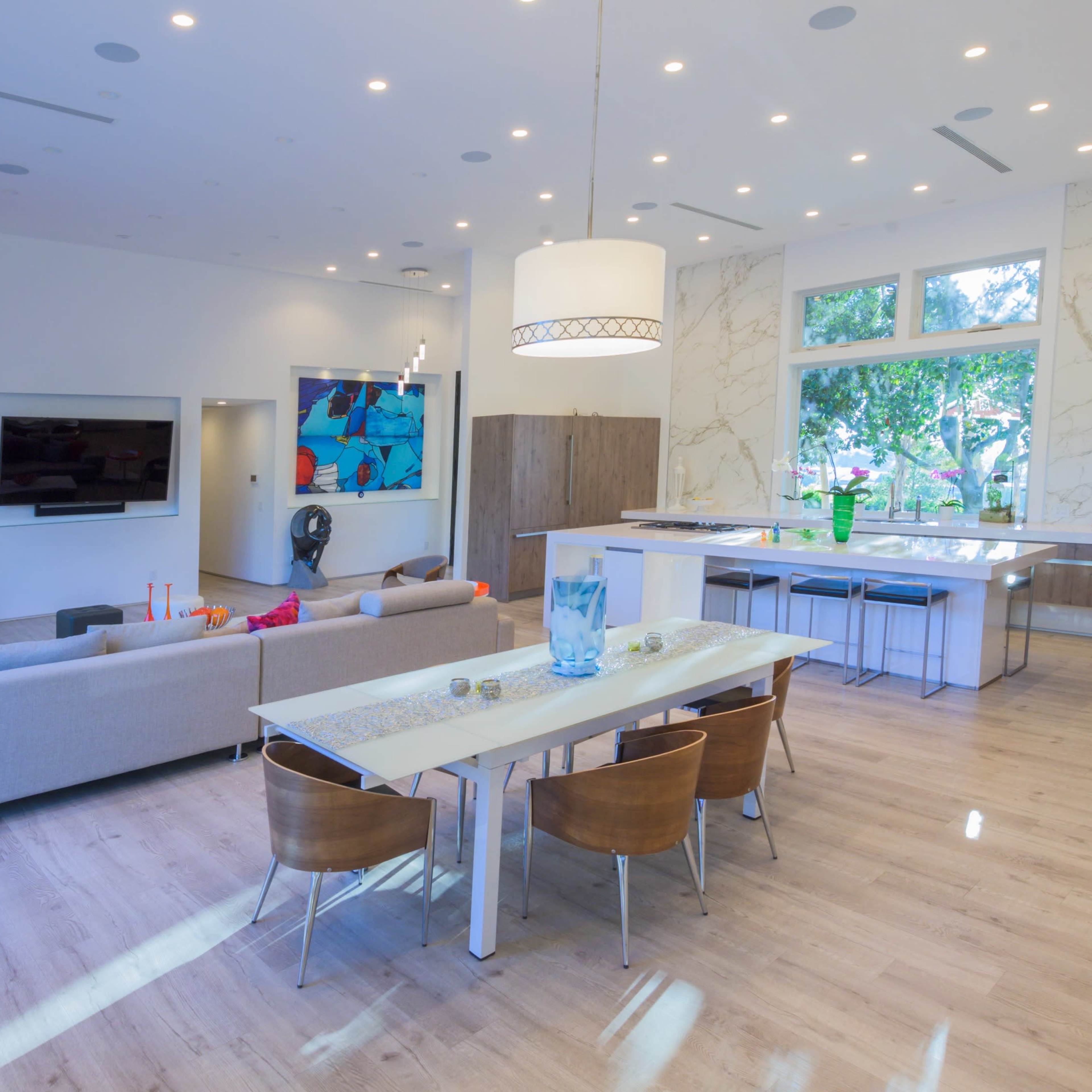 A modern open-concept living and dining area with a large kitchen island, wooden dining chairs, and large windows that let in natural light.