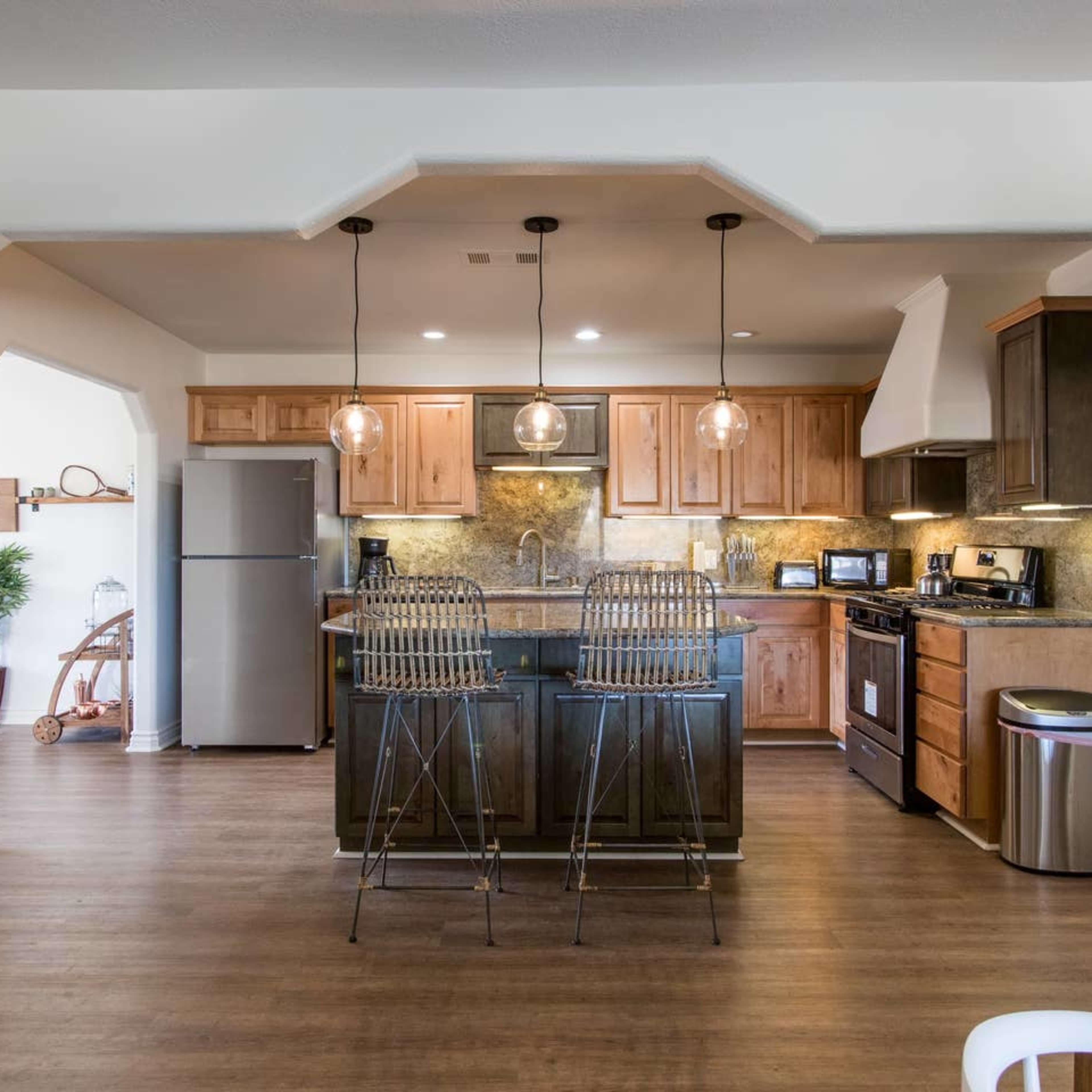 A modern kitchen with wooden cabinetry, stainless steel appliances, and a bar area with two stools.