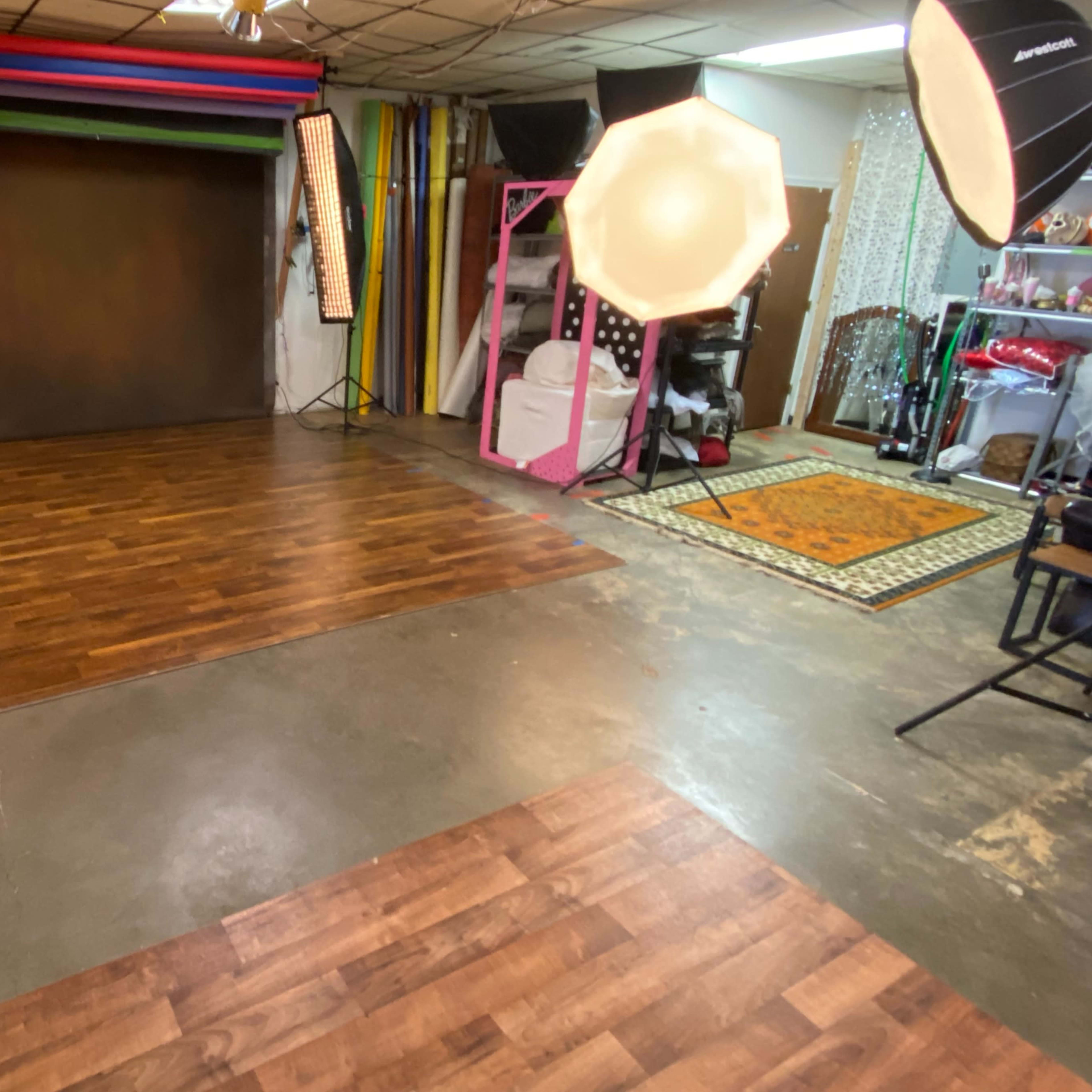 A photography studio with a wooden floor, backdrop setup, and various lighting equipment arranged in the space.
