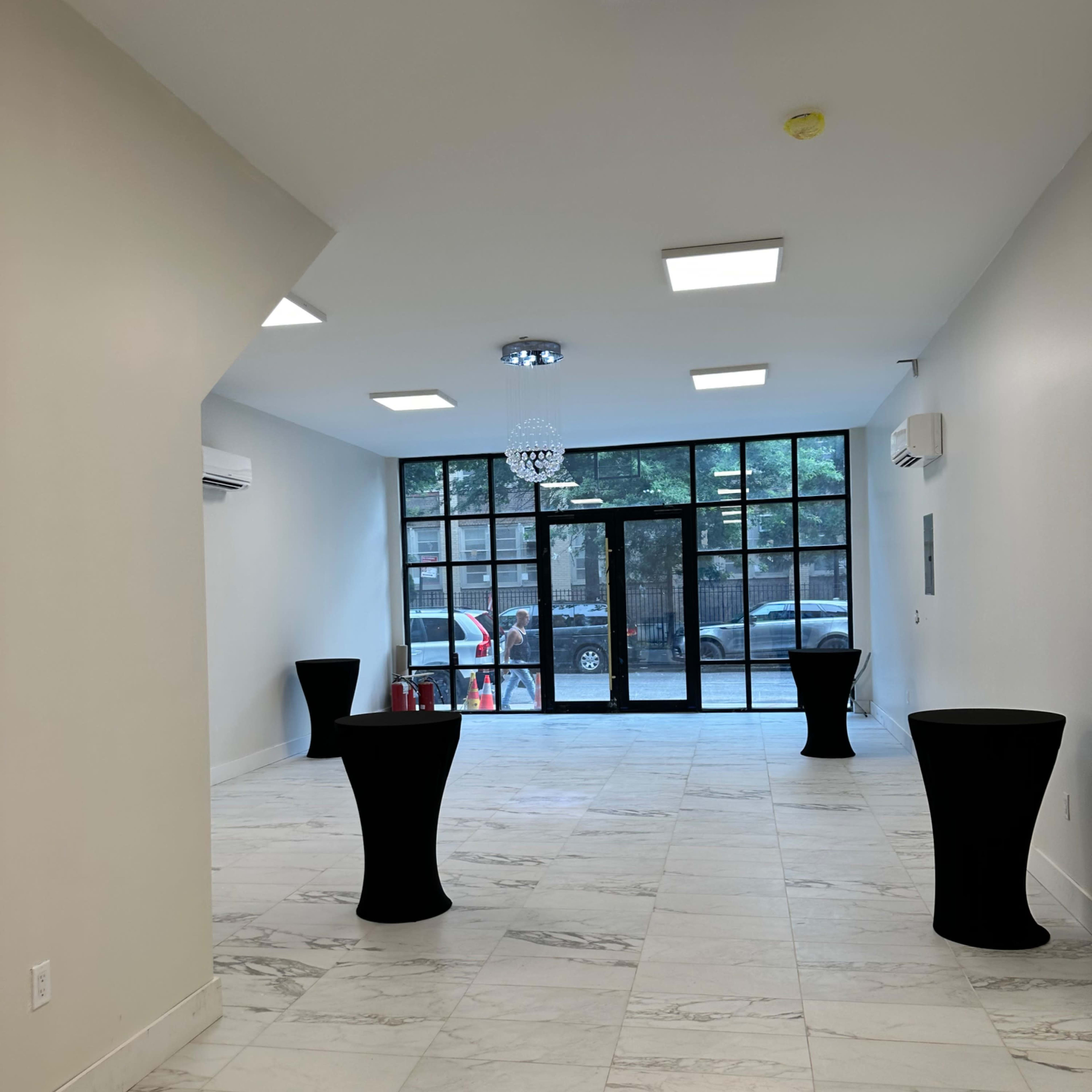 A spacious, well-lit interior with polished marble floors, large windows, and two tall black tables.