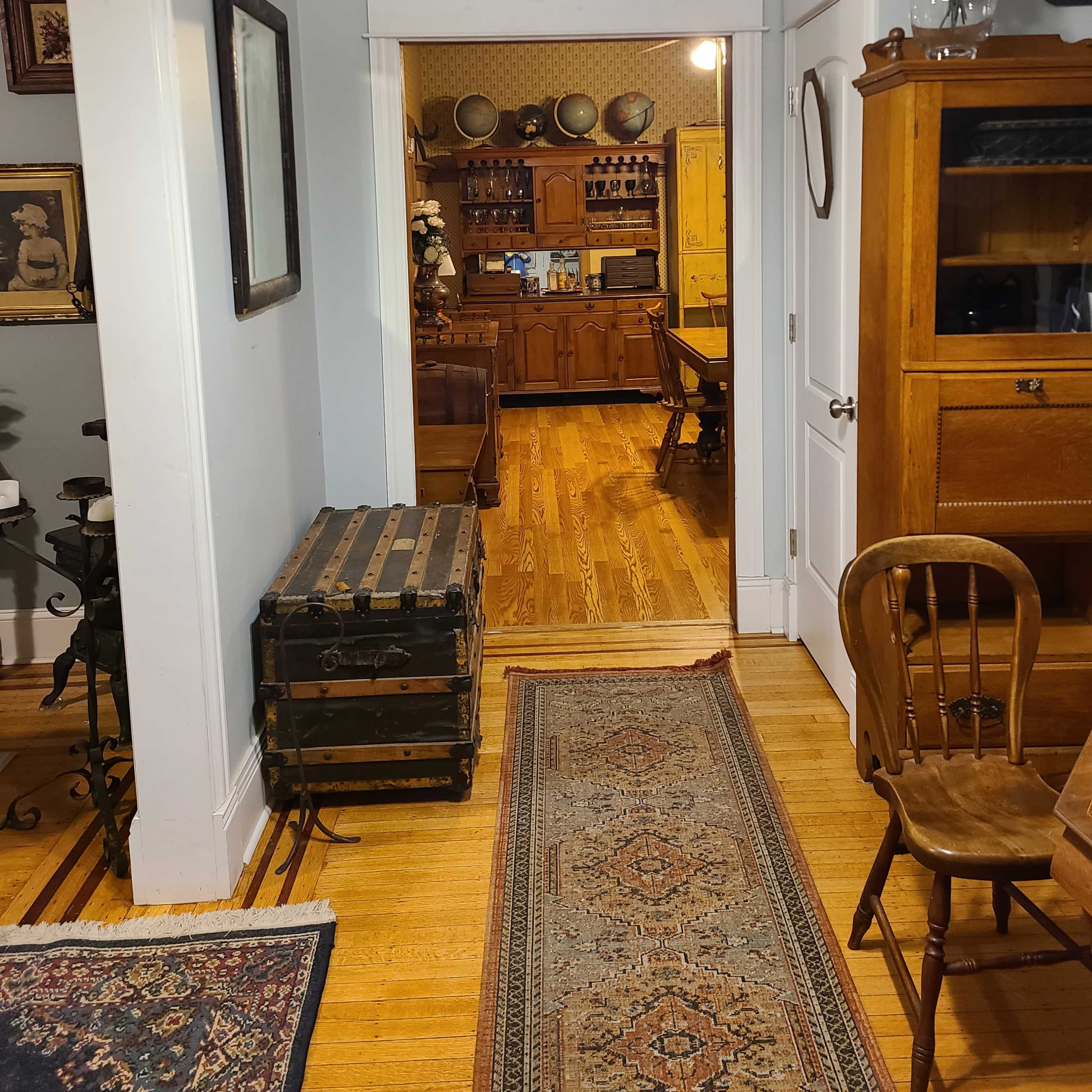A bright hallway leading to a rustic kitchen area with wooden furniture and decorative plates on the walls.