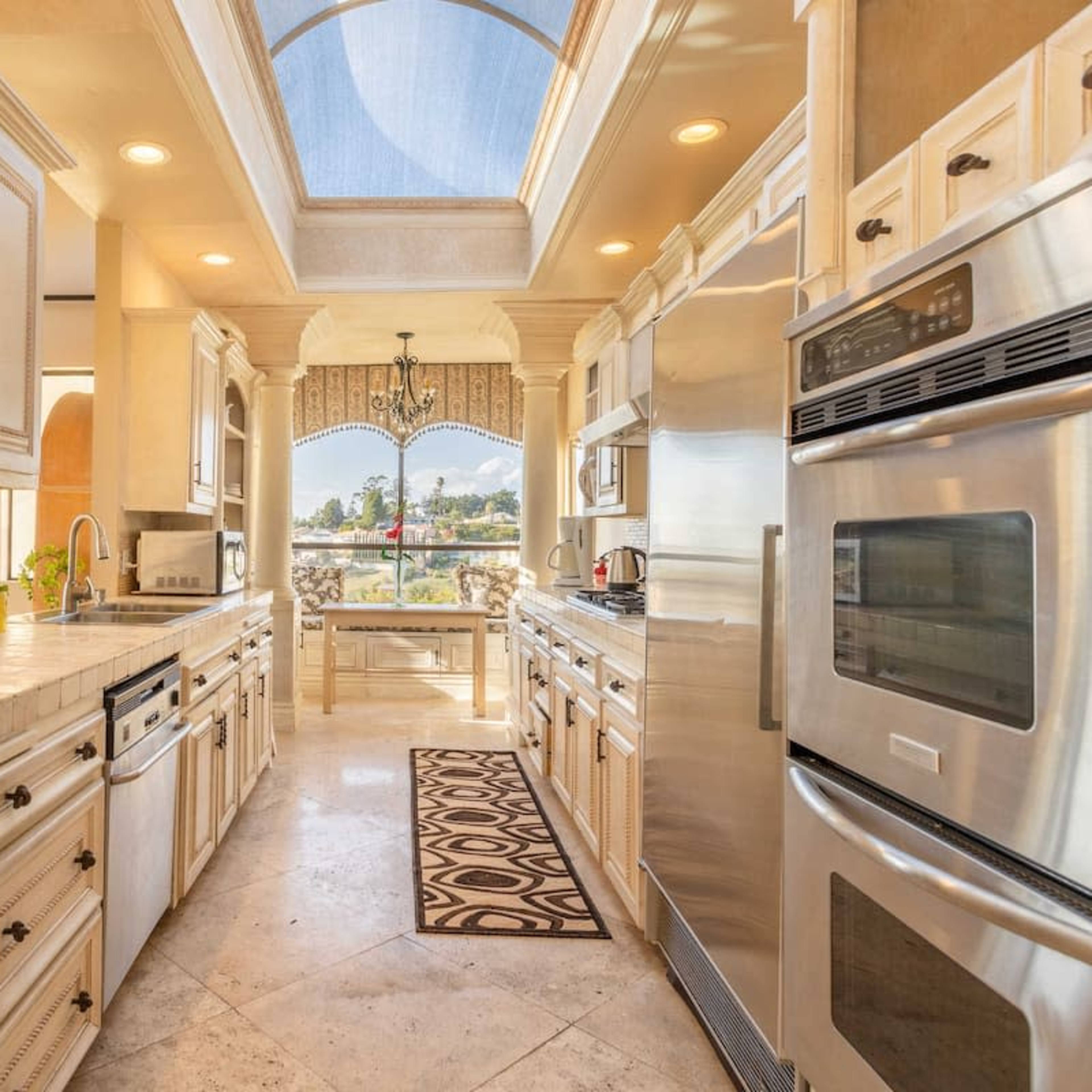 A spacious kitchen with cream-colored cabinets, stainless steel appliances, and a central island, illuminated by natural light from a skylight.