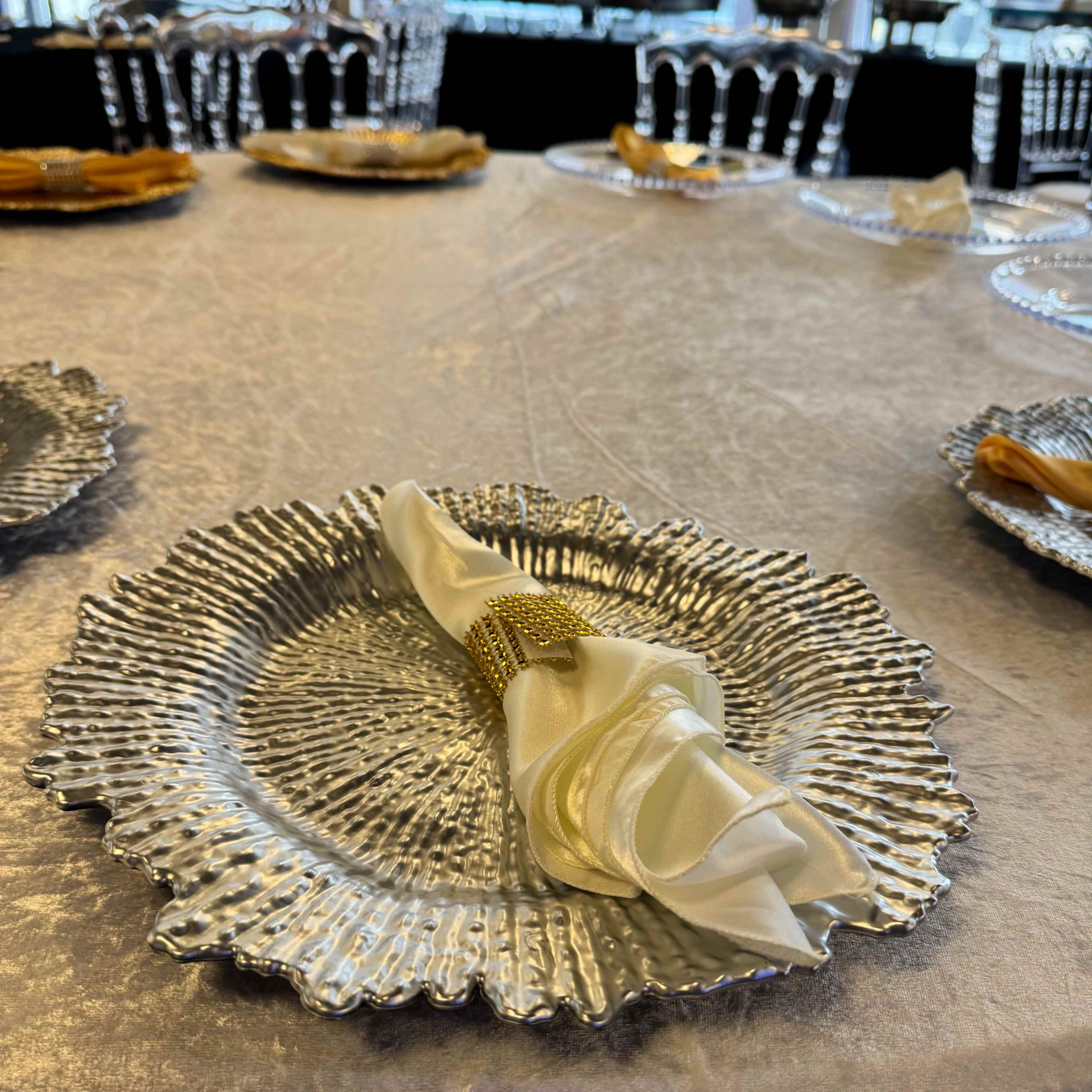 A table set for a formal event, featuring silver decorative plates with neatly arranged napkins and cutlery.
