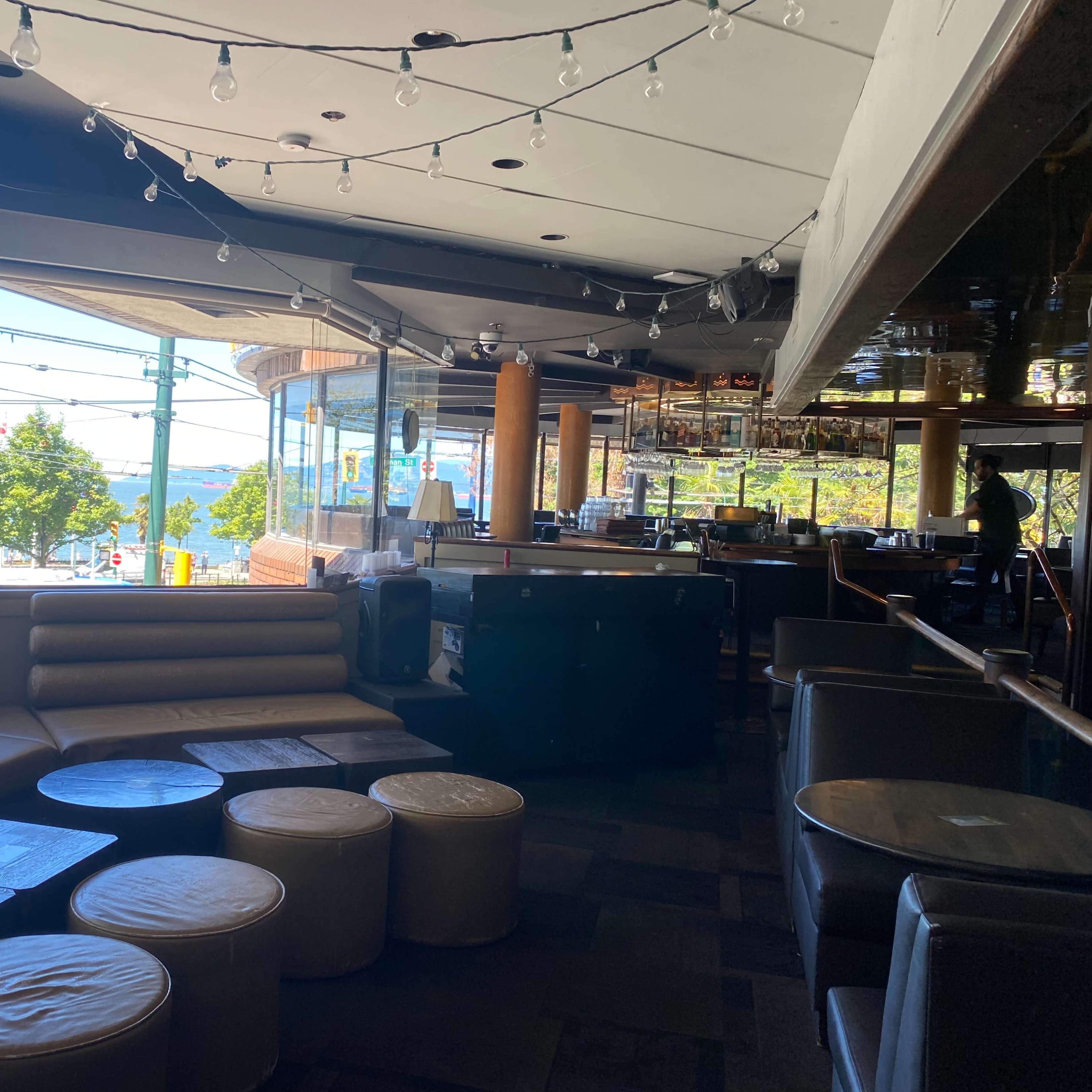 The interior of a restaurant or bar with a seating area, circular tables, and large windows overlooking a view outside.