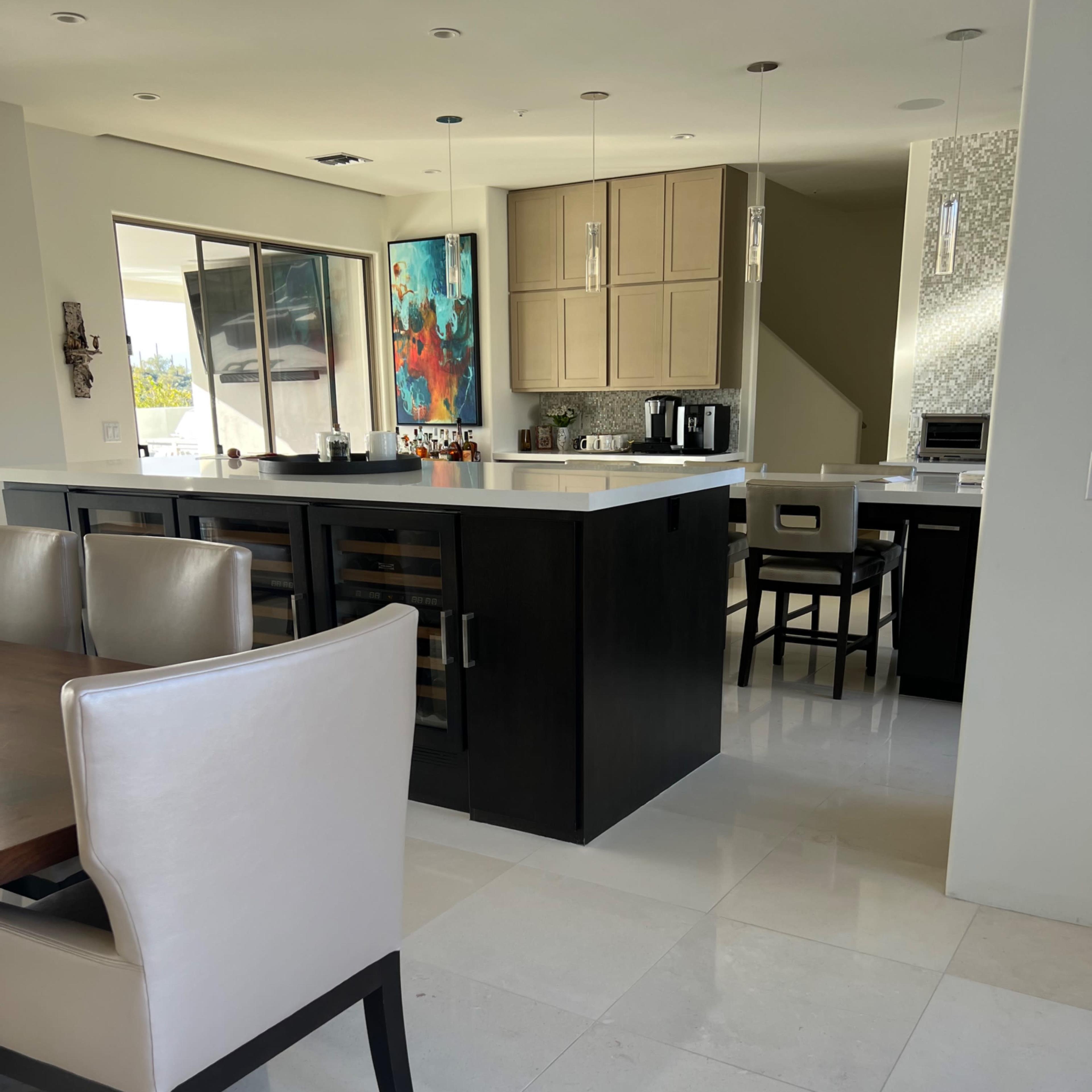 A modern kitchen with a dining area featuring a large table and upholstered chairs, alongside a sleek kitchen island and appliances.