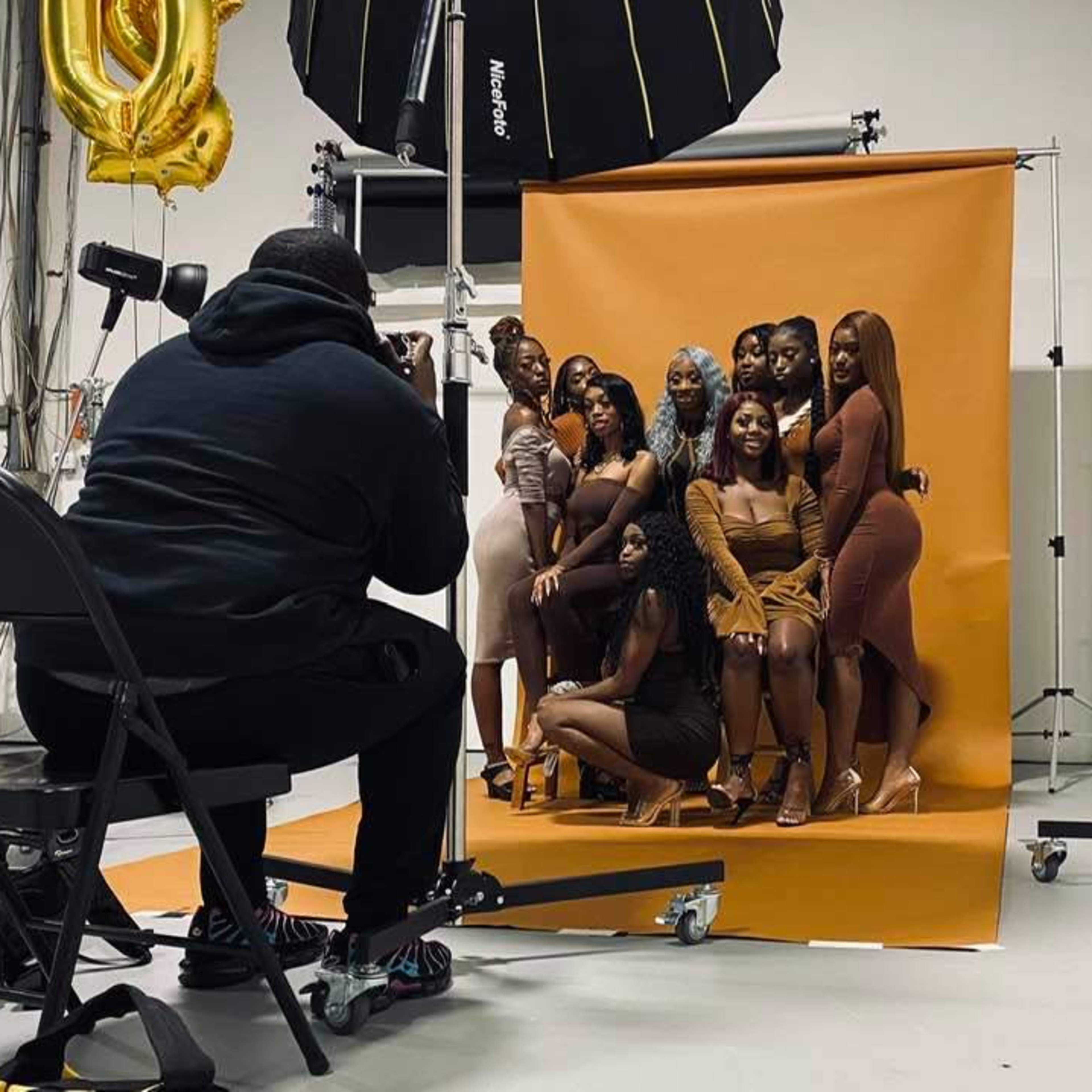A photographer captures a posed group of women in front of an orange backdrop in a studio setting.