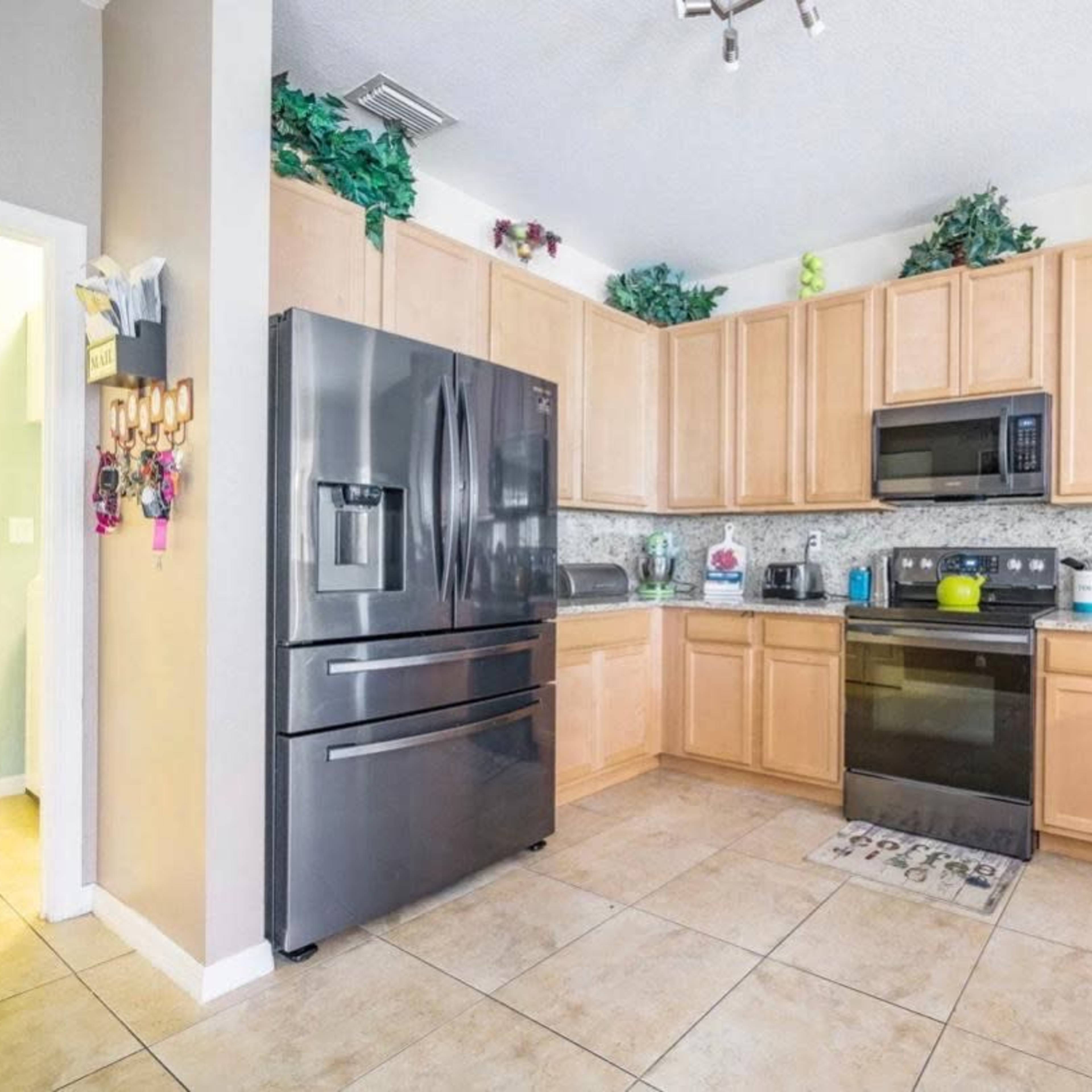 A kitchen with wooden cabinets, black appliances, and a tiled floor, featuring organized countertops and decorative plants.