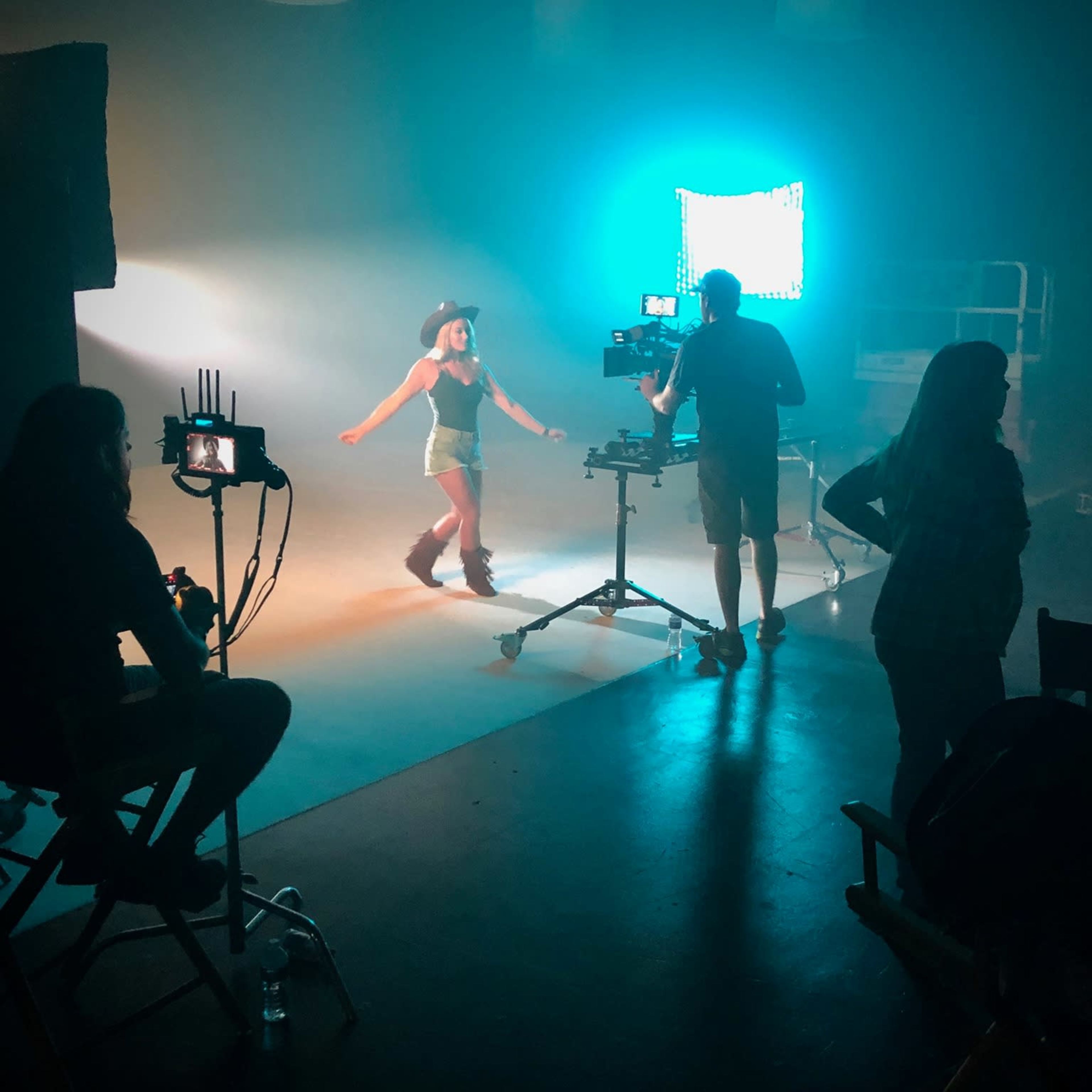A woman dances on set while a crew works with cameras and lighting equipment in a film studio.