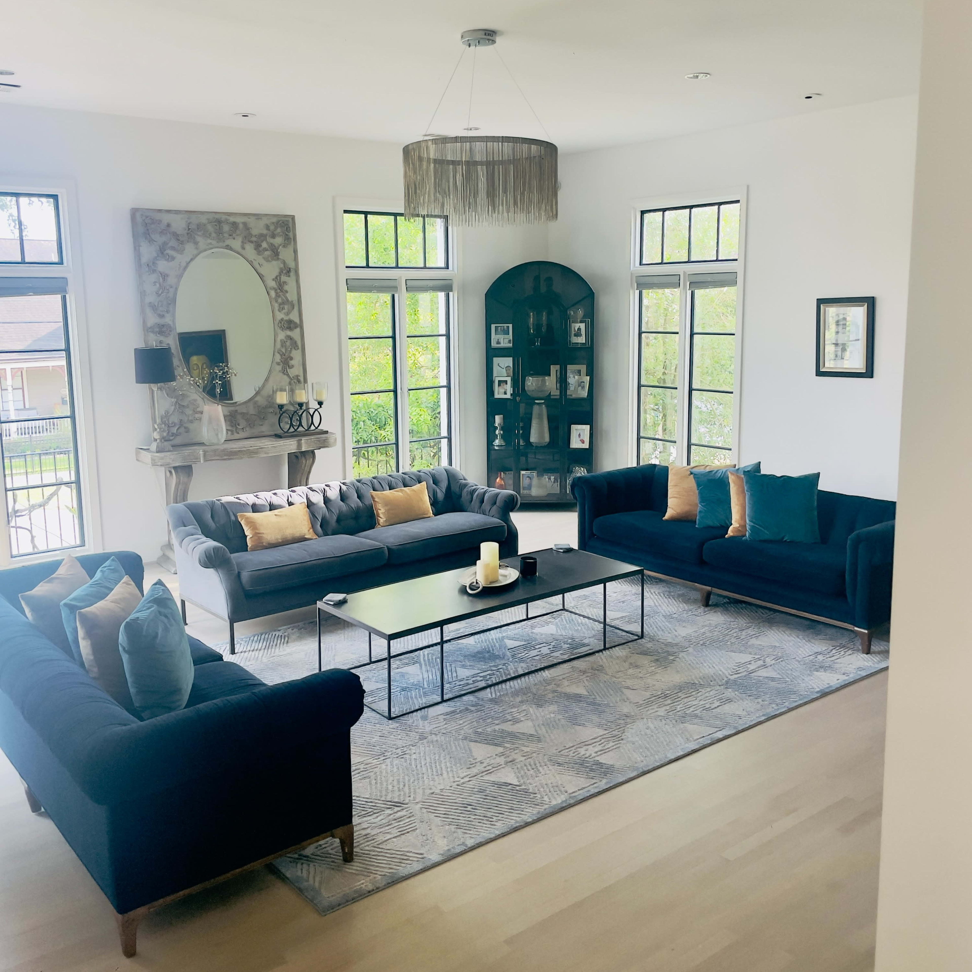 A modern living room features two dark sofas, a central glass coffee table, and large windows allowing light to fill the space.