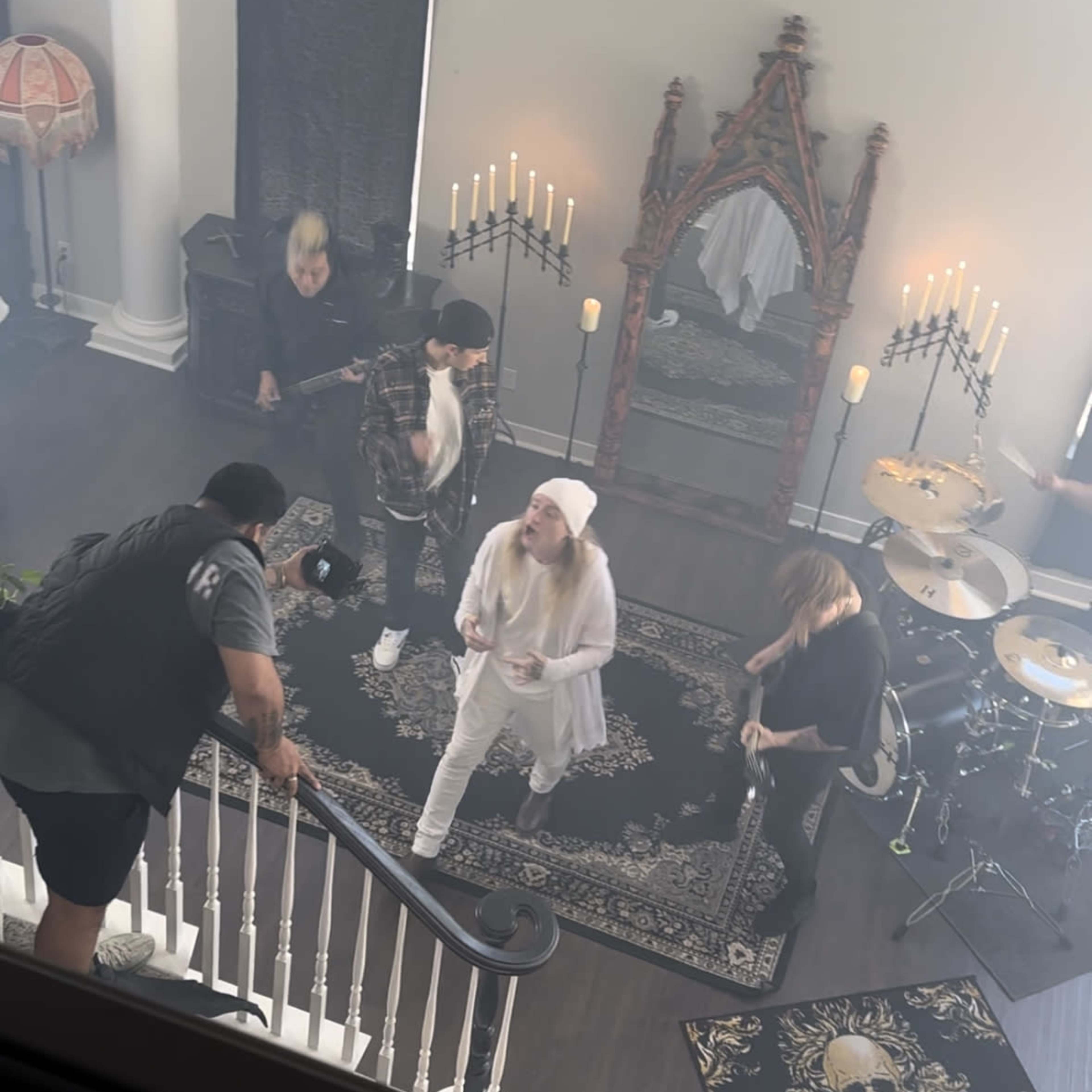 A group of musicians performs on a stage set in a decorated room with candles and gothic elements.