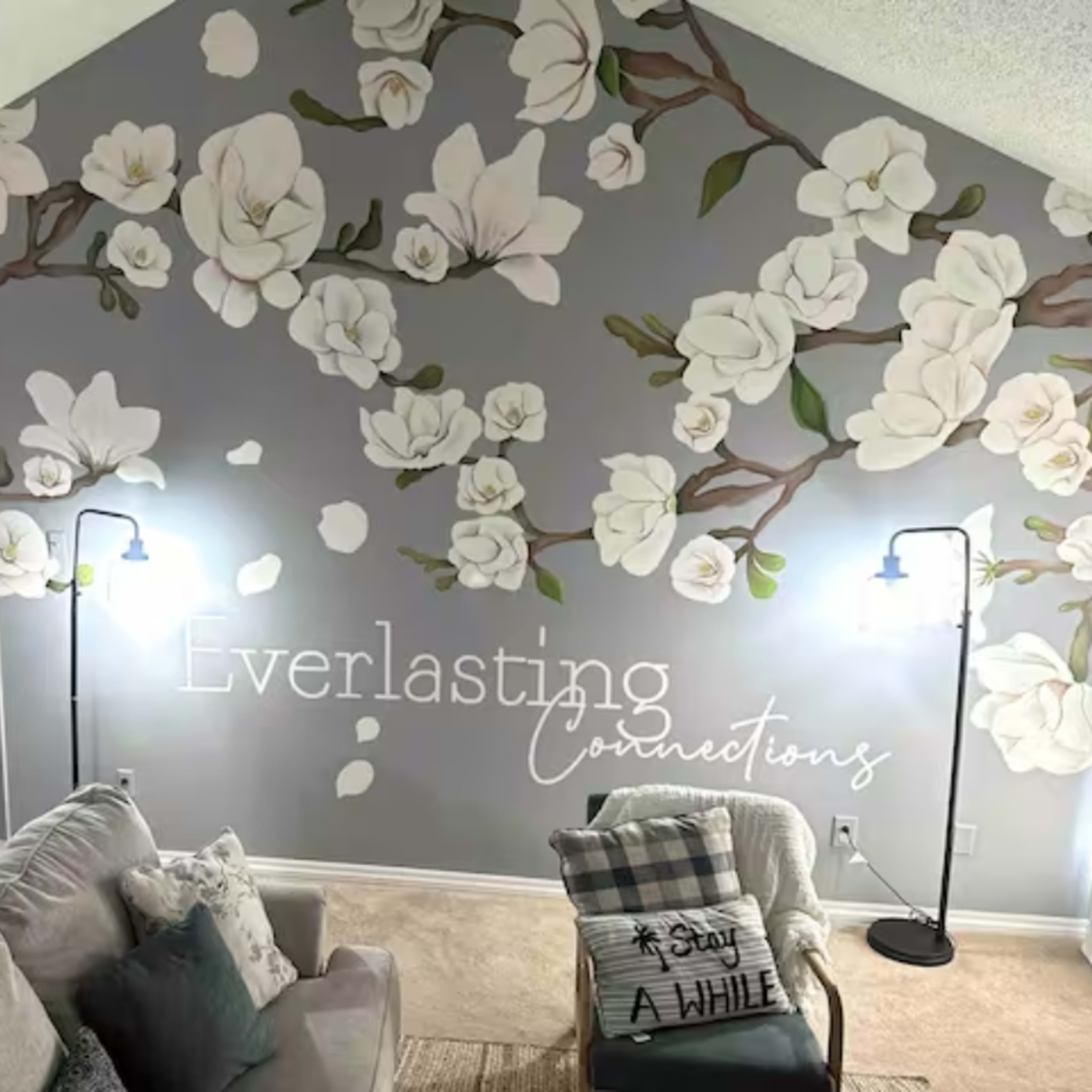 A living room features a large mural of white flowers on a grey wall, accompanied by a couch and decorative items.