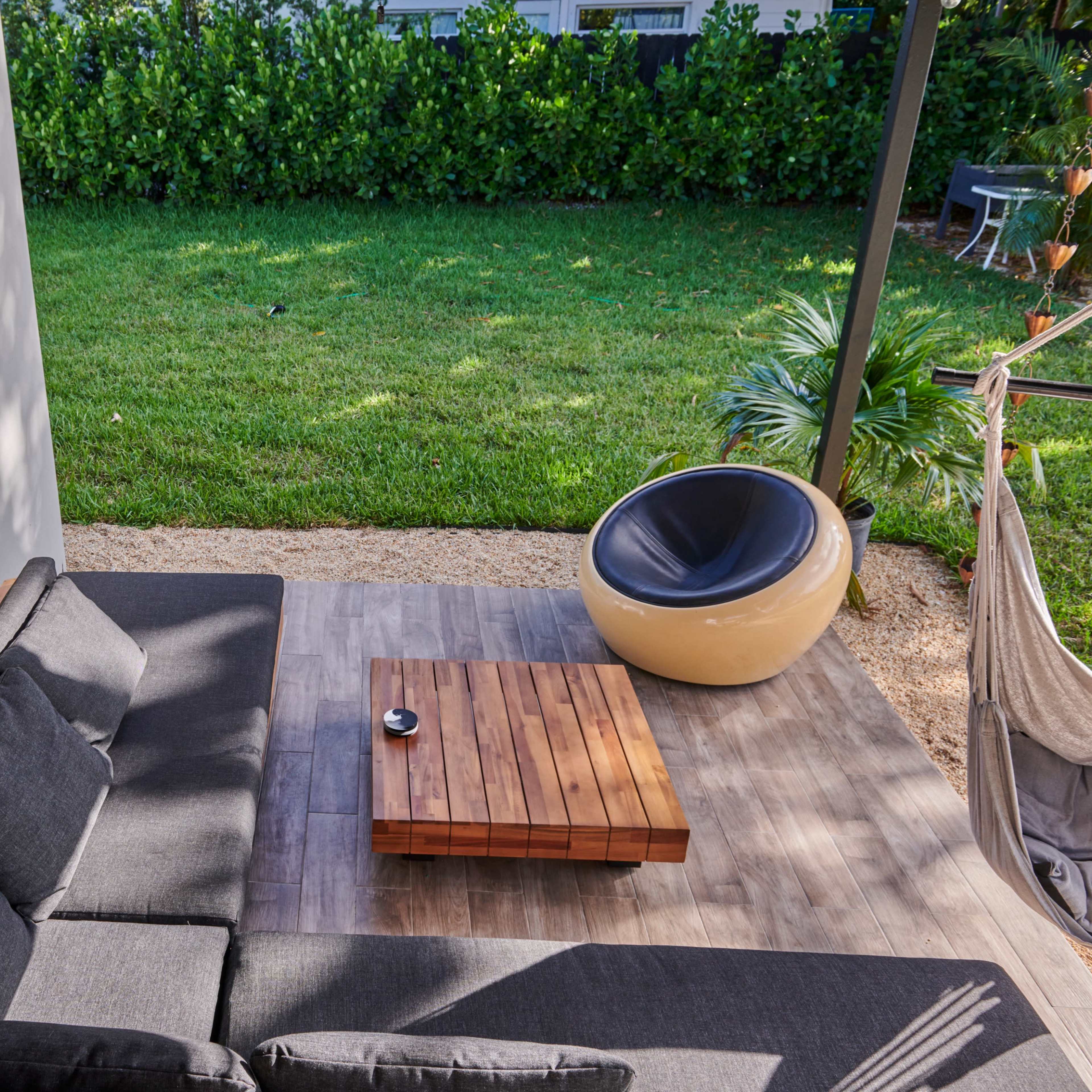 A patio area features a gray sectional sofa and a wooden coffee table, with a grassy yard and plants in the background.