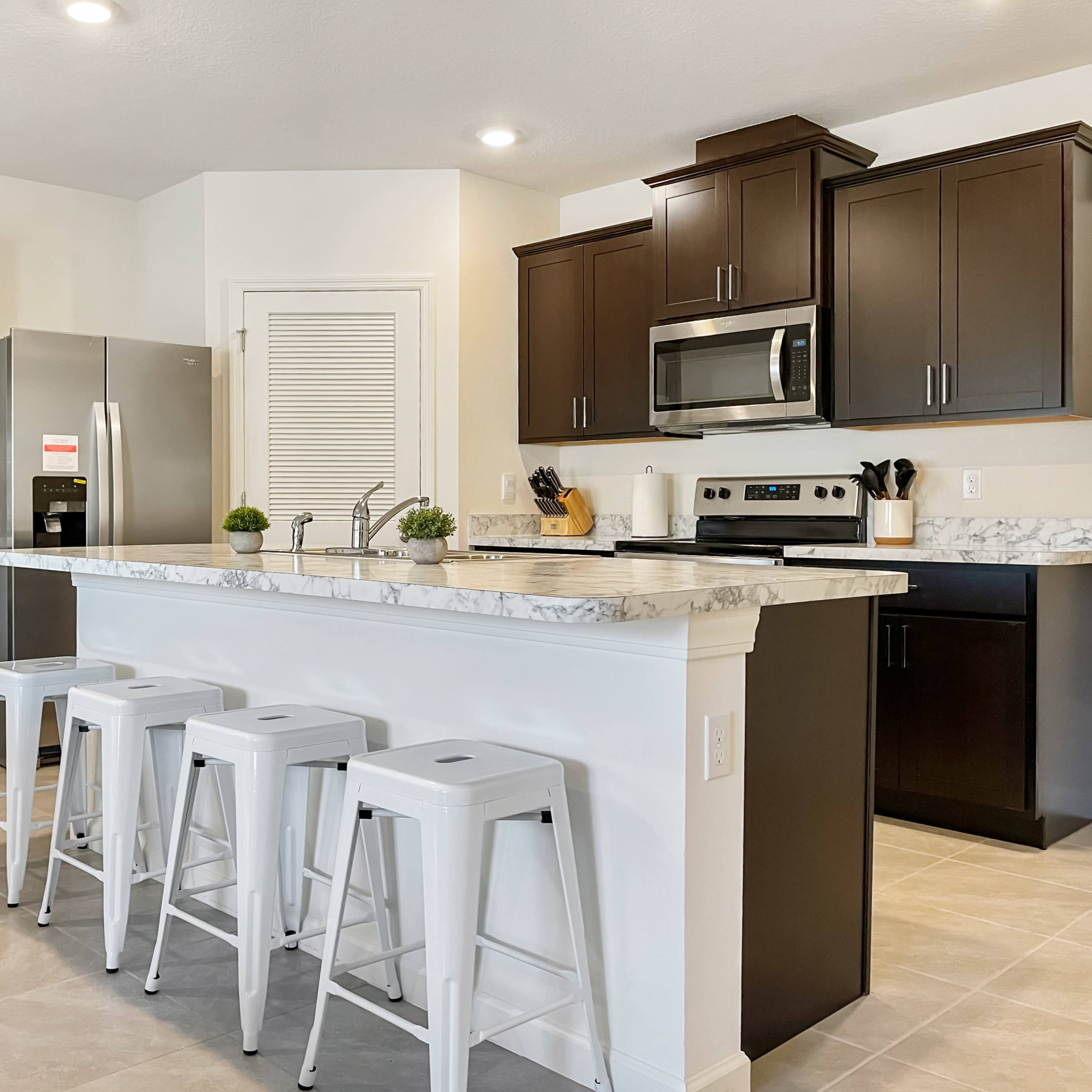 A modern kitchen features dark wood cabinetry, stainless steel appliances, and a marble countertop island with white stools.