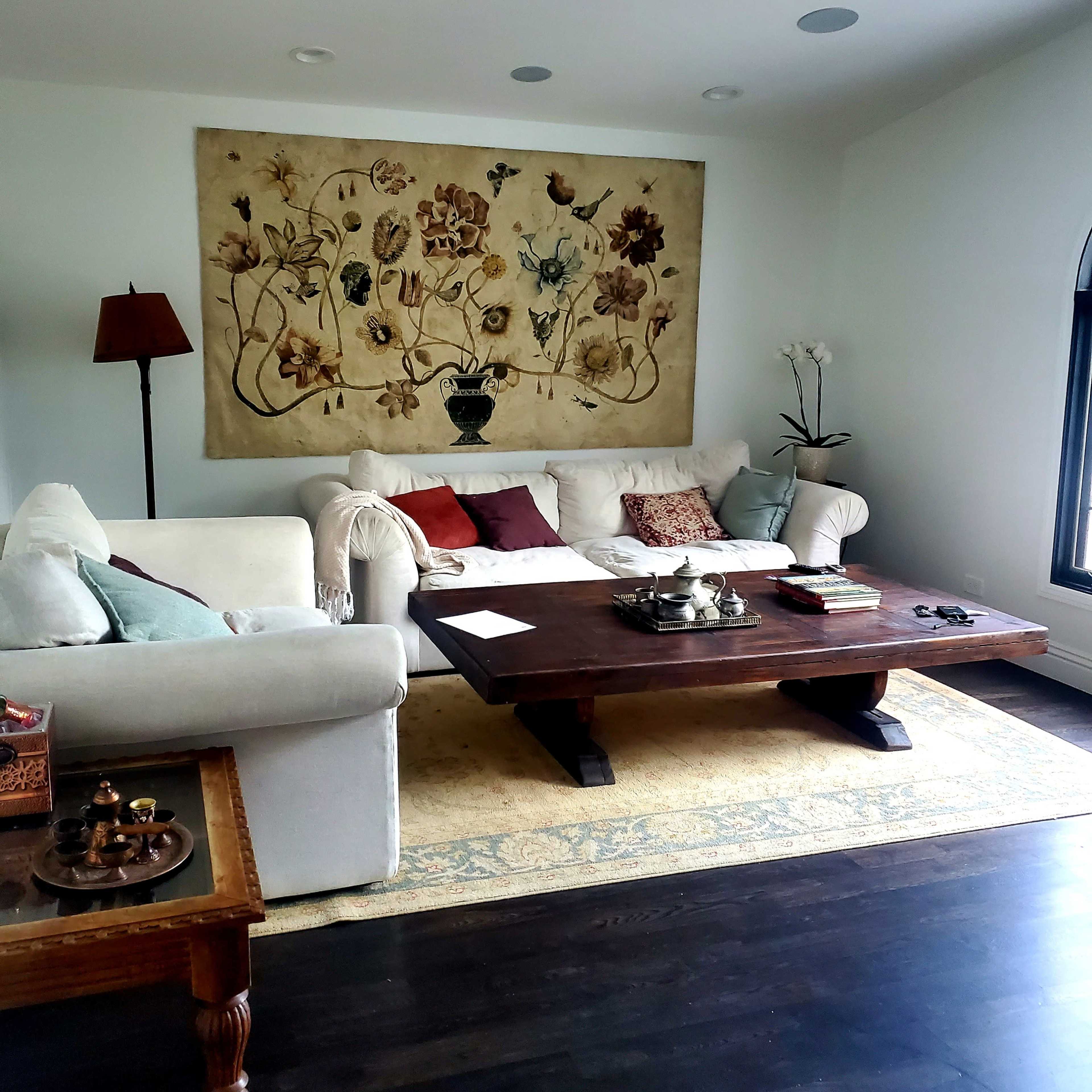 A living room with a white couch, a wooden coffee table, an ornate wall hanging, and a lamp in the corner.