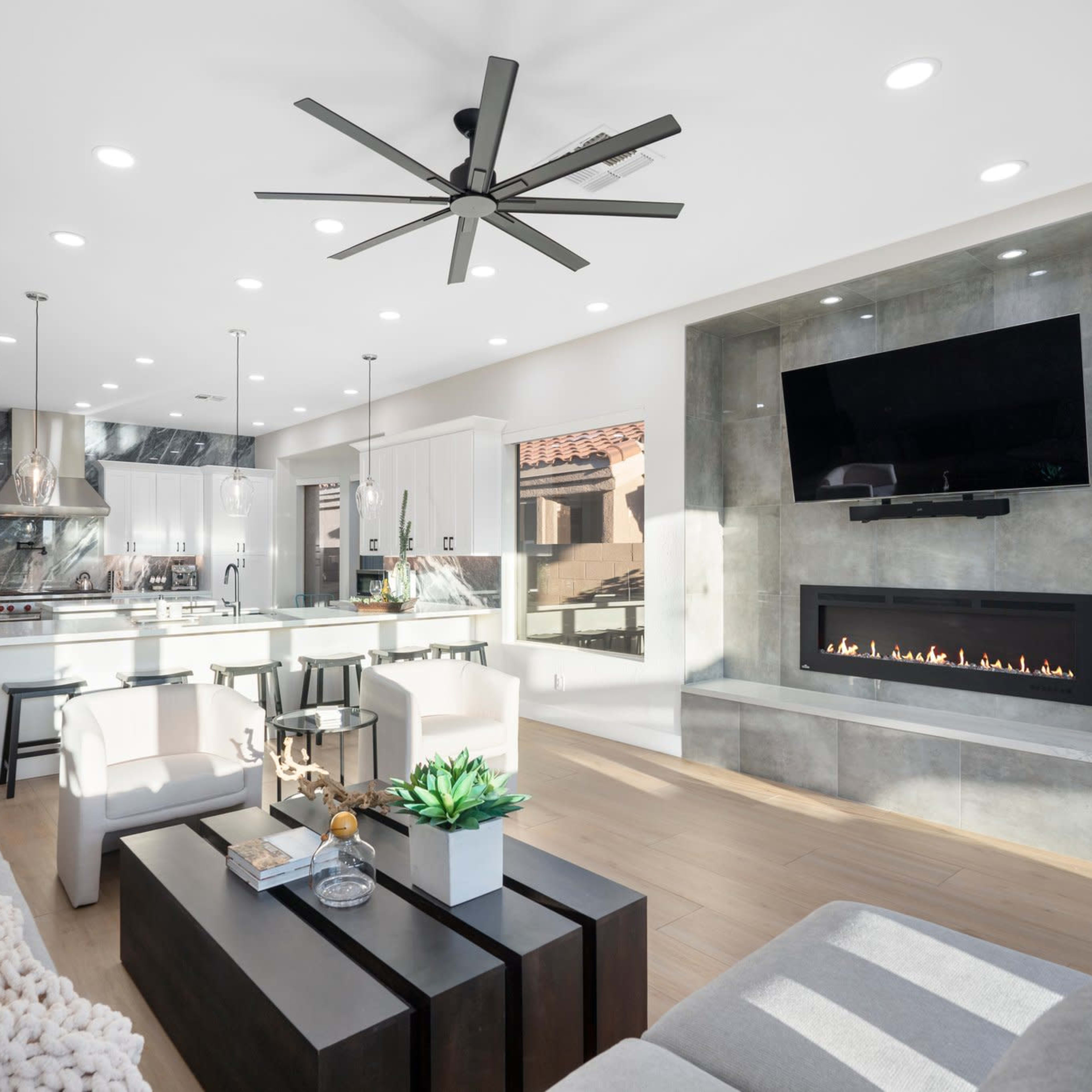 The modern living room features a sleek design with a fireplace, a large television mounted on the wall, and a spacious kitchen in the background.