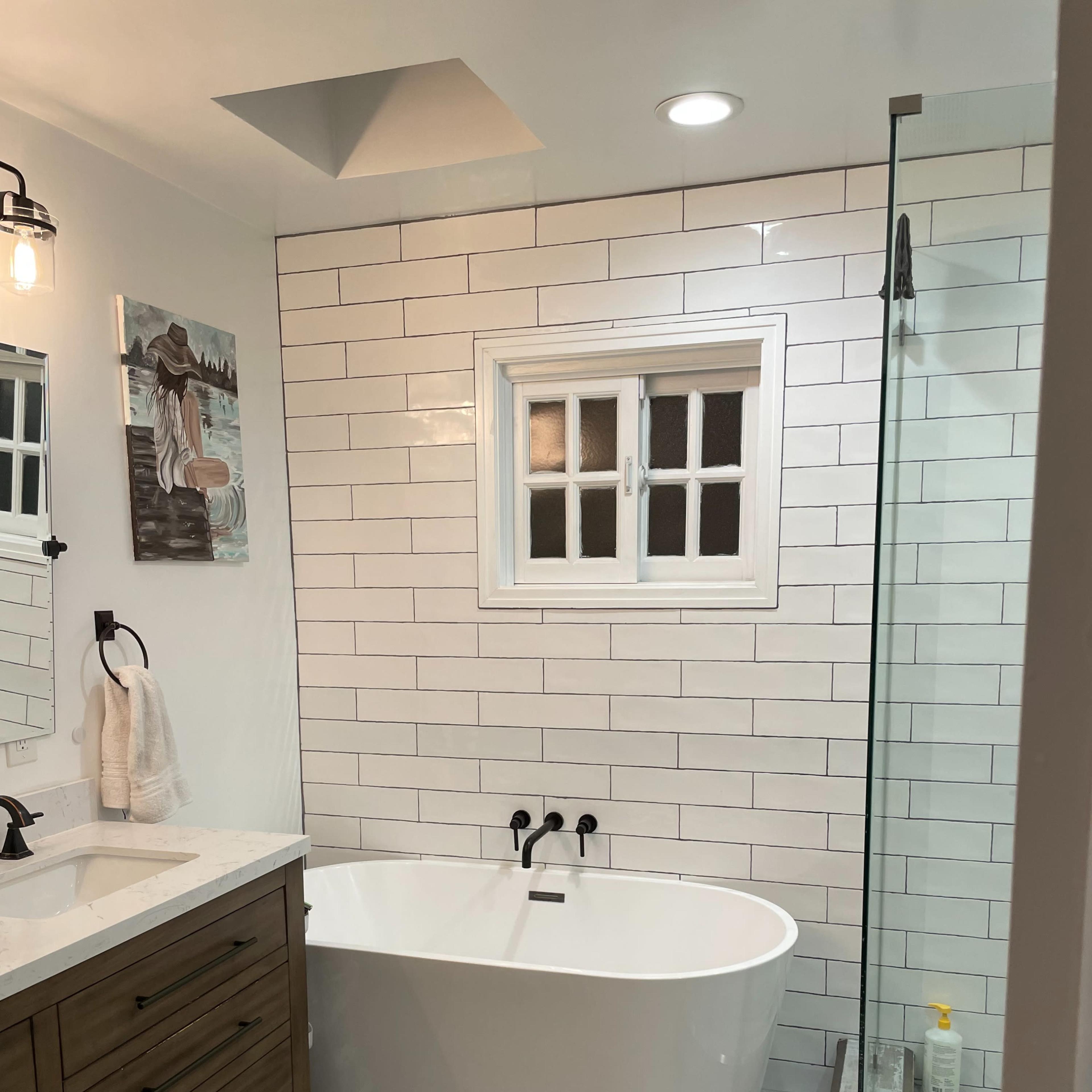 A modern bathroom featuring a freestanding tub, a glass shower enclosure, white tiled walls, and a wooden vanity with a sink.
