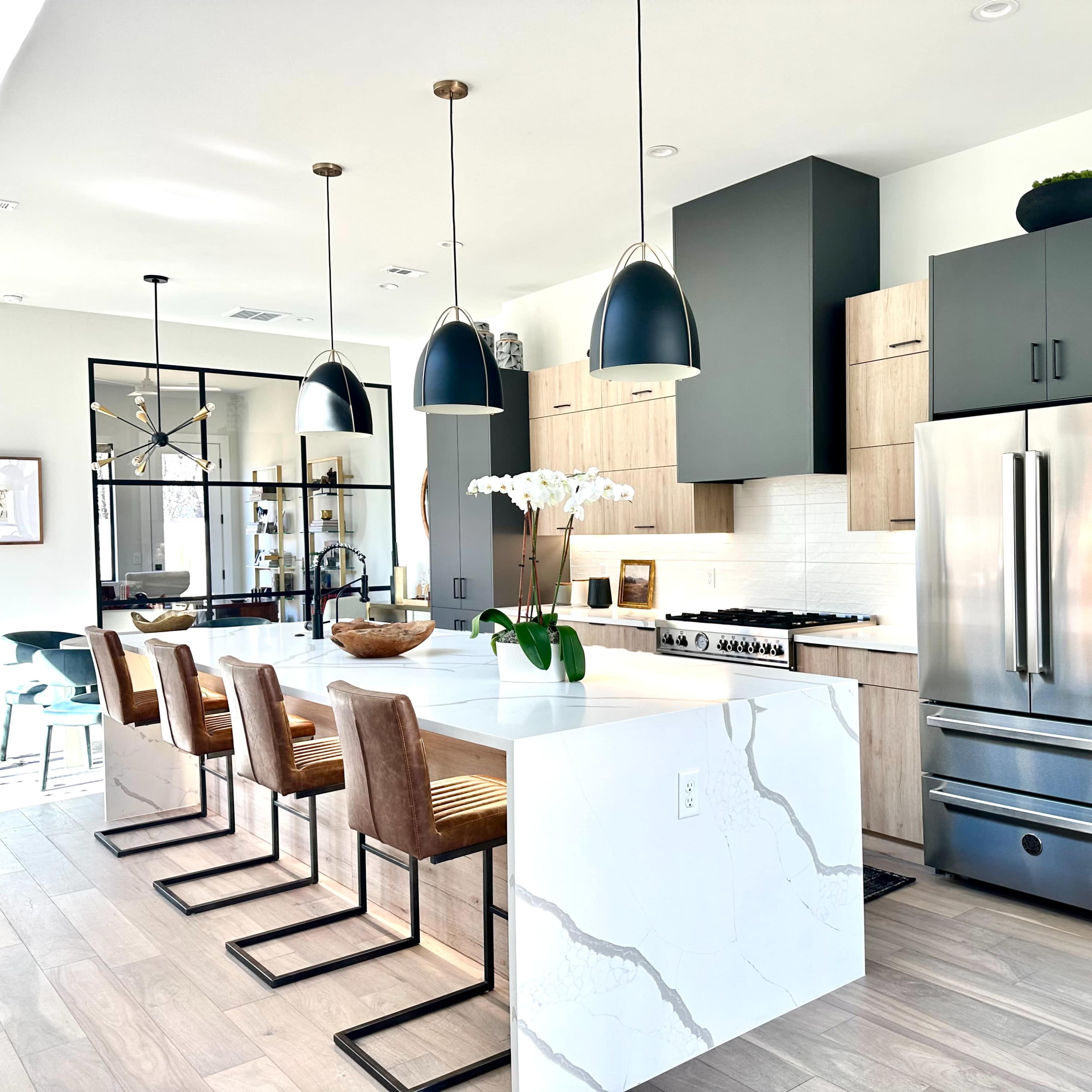 A modern kitchen featuring a large island with four stools, stainless steel appliances, and pendant lighting, complemented by light wood and dark cabinetry.