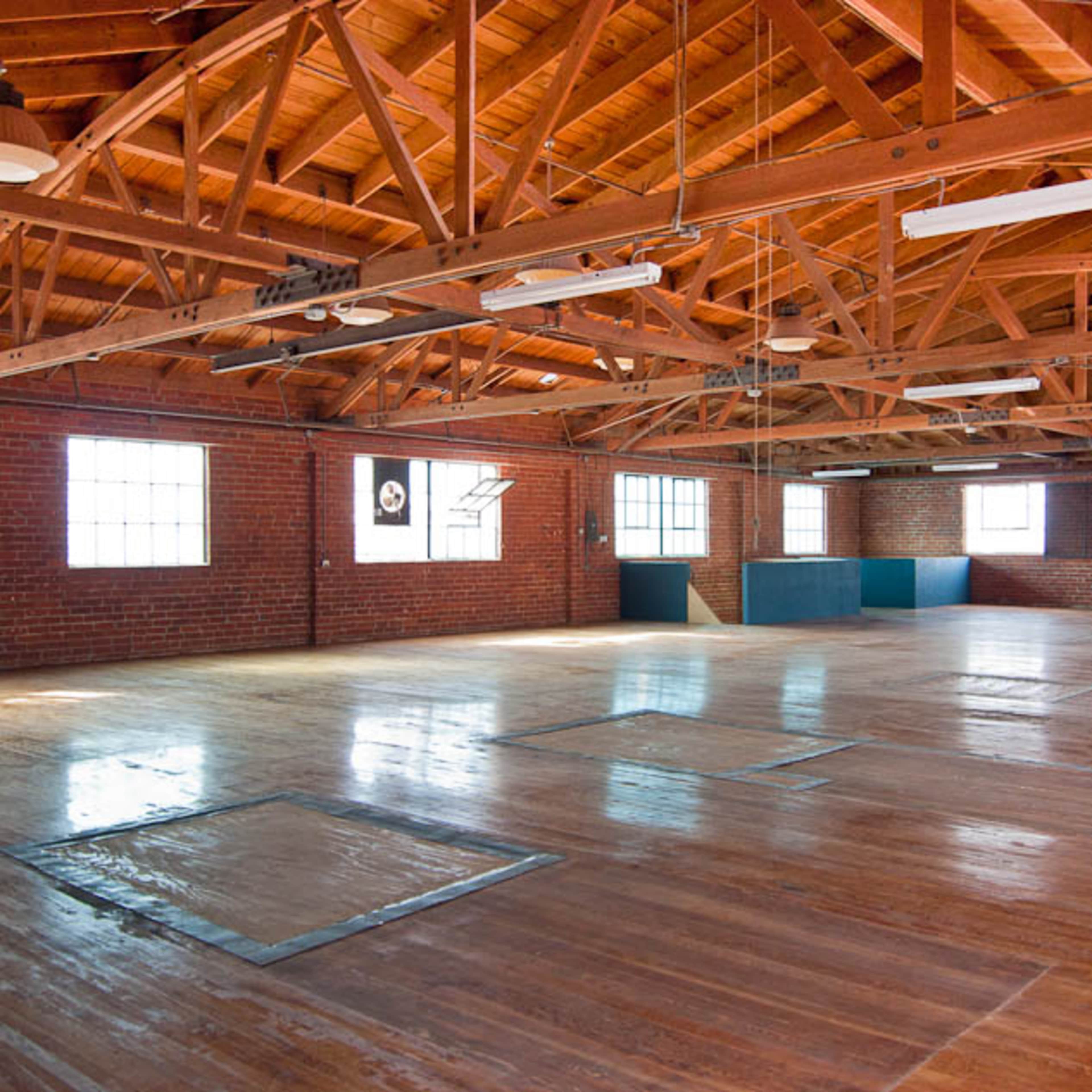 A spacious, empty warehouse interior with polished wooden floors and exposed wooden beams supporting the ceiling.