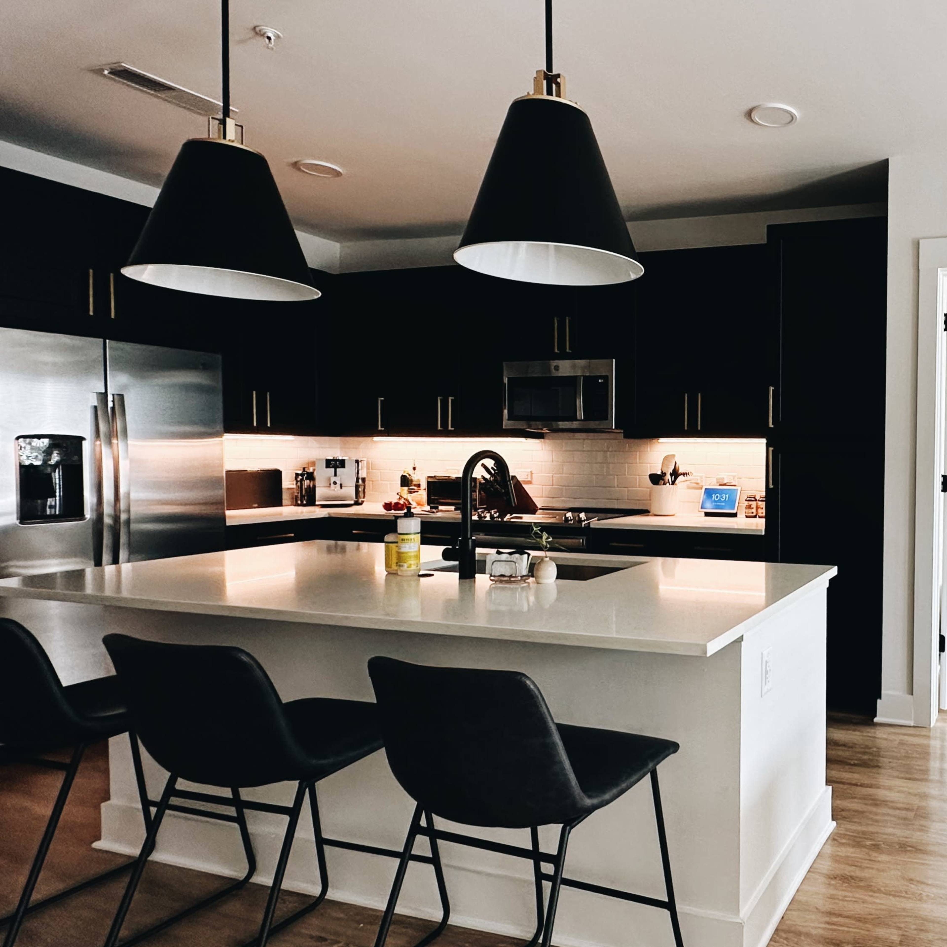 A modern kitchen with a large island, black cabinetry, and a doorway leading to a bright living area with a white sofa.