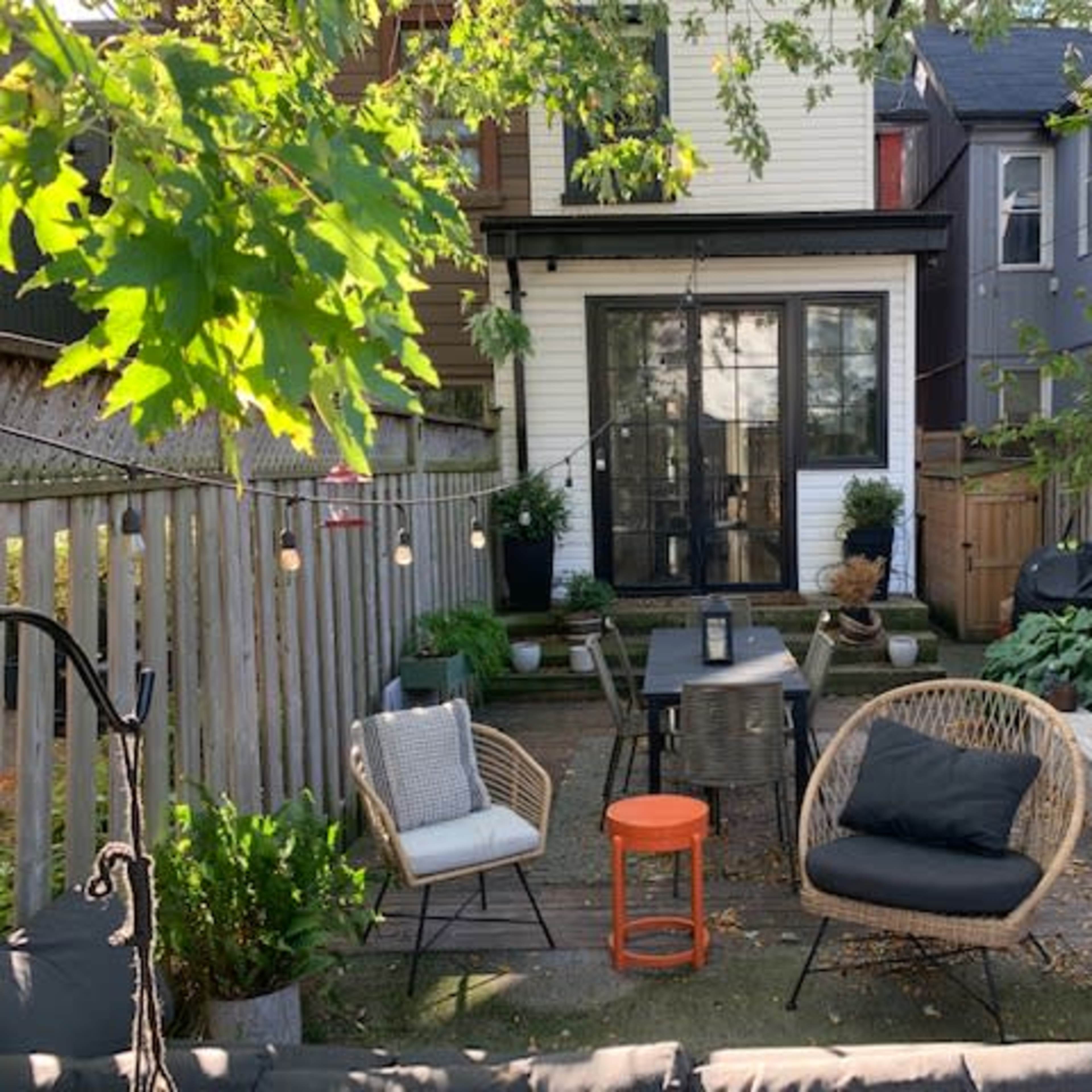 A back patio with a table and chairs surrounded by plants, leading to a house with a large glass sliding door.