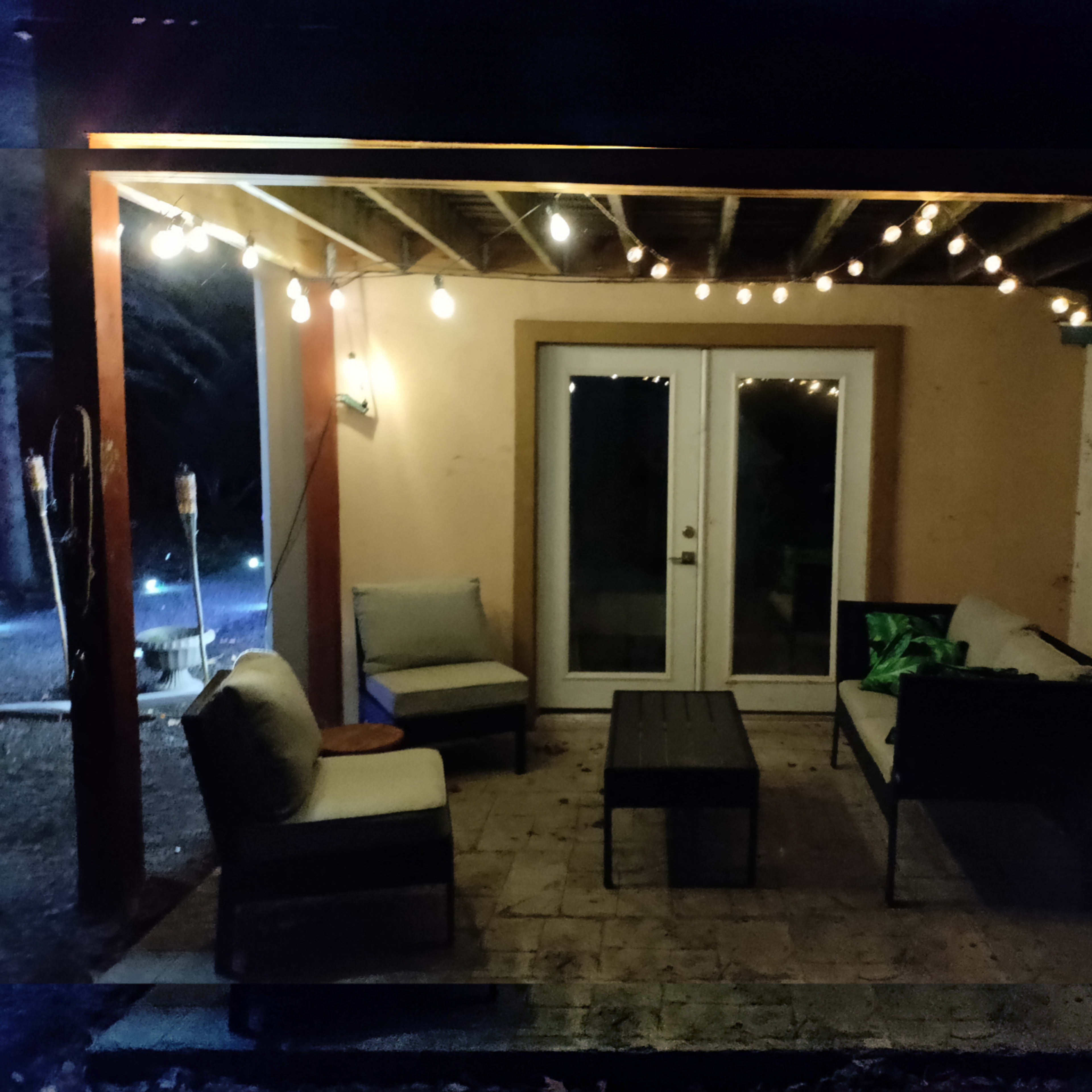 A covered patio area features string lights, a table, and seating arranged around it.