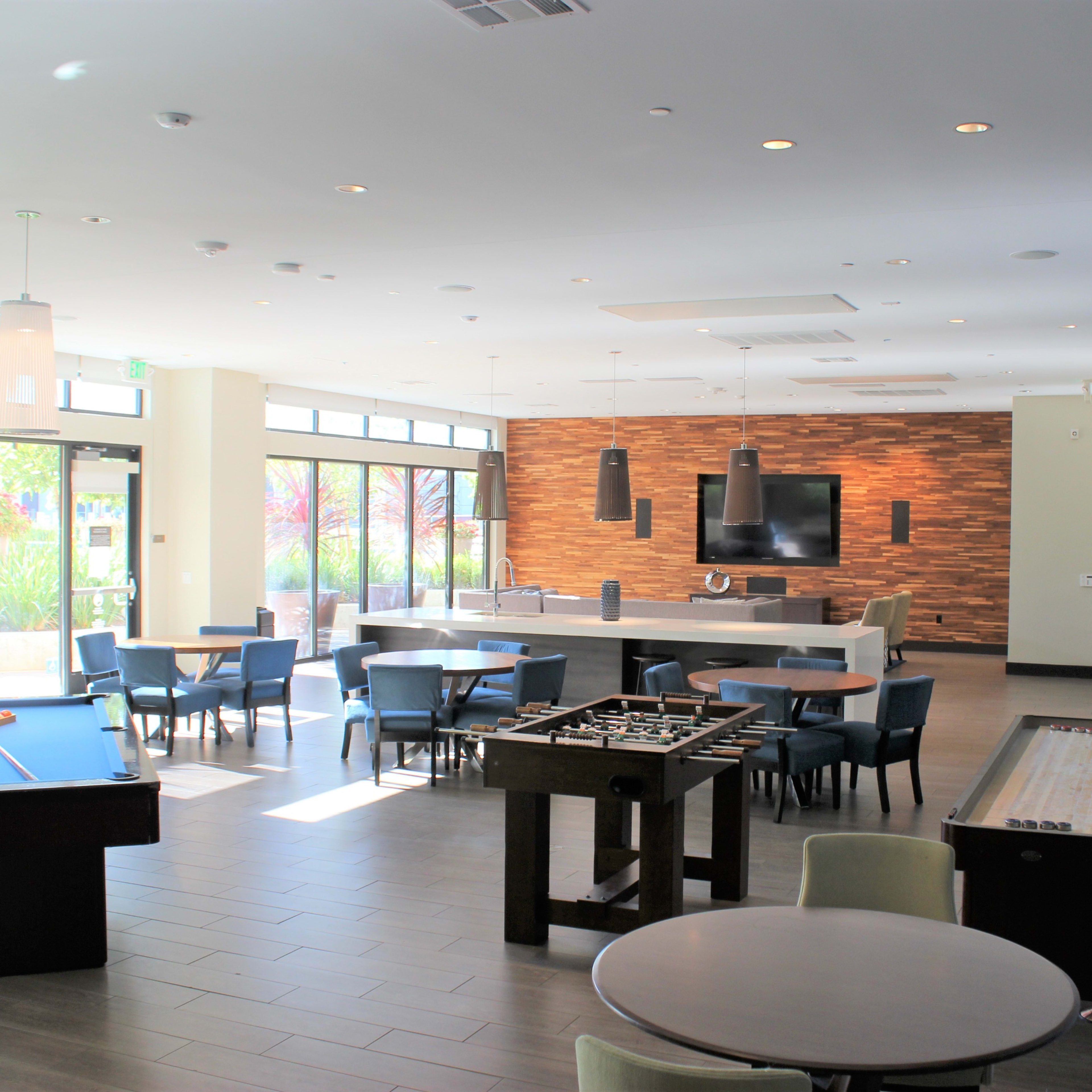 A modern recreational room with a pool table, foosball table, and several seating areas, featuring large windows that provide natural light.