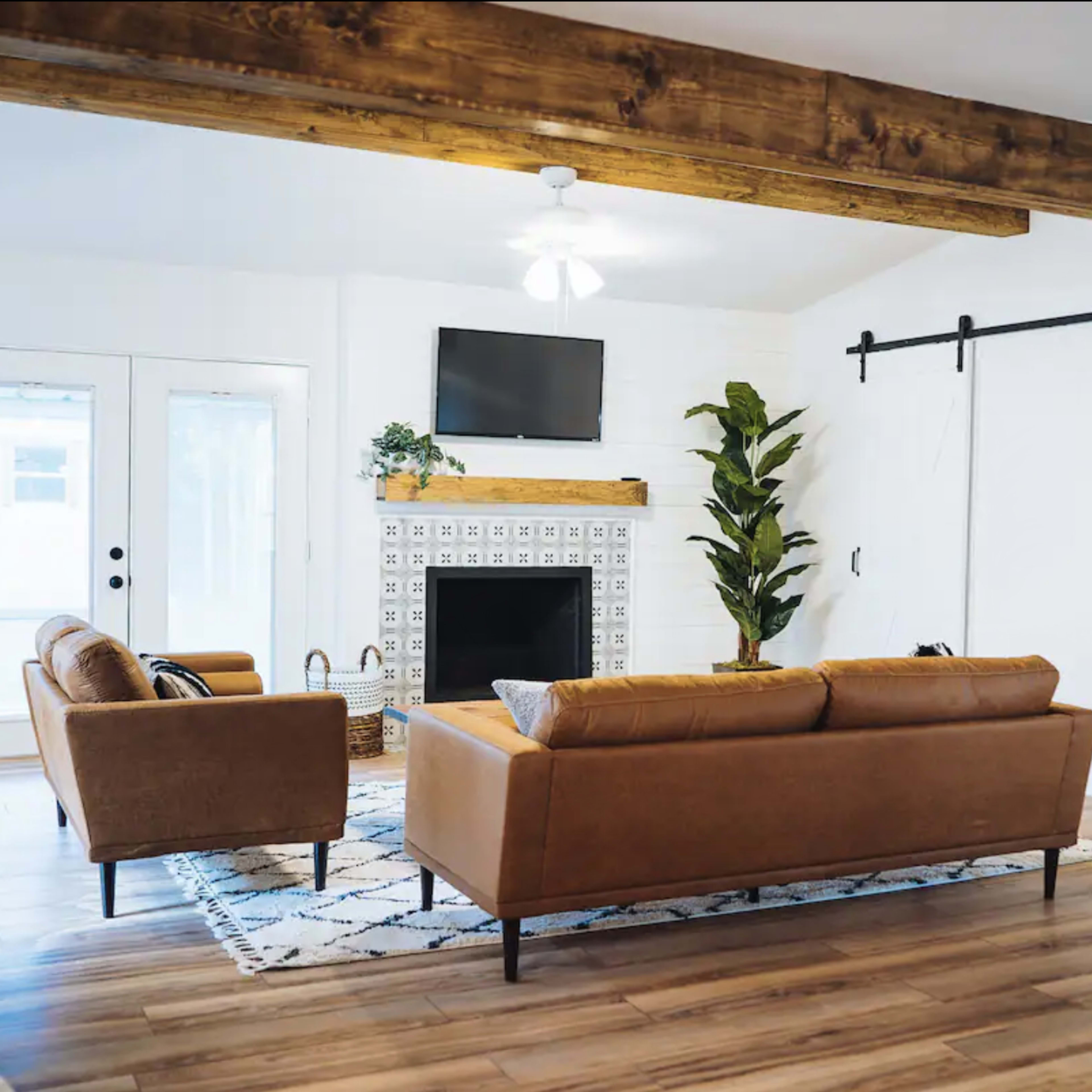 The living room features two leather sofas facing a decorative fireplace with a television mounted above it, and large sliding doors leading outside.