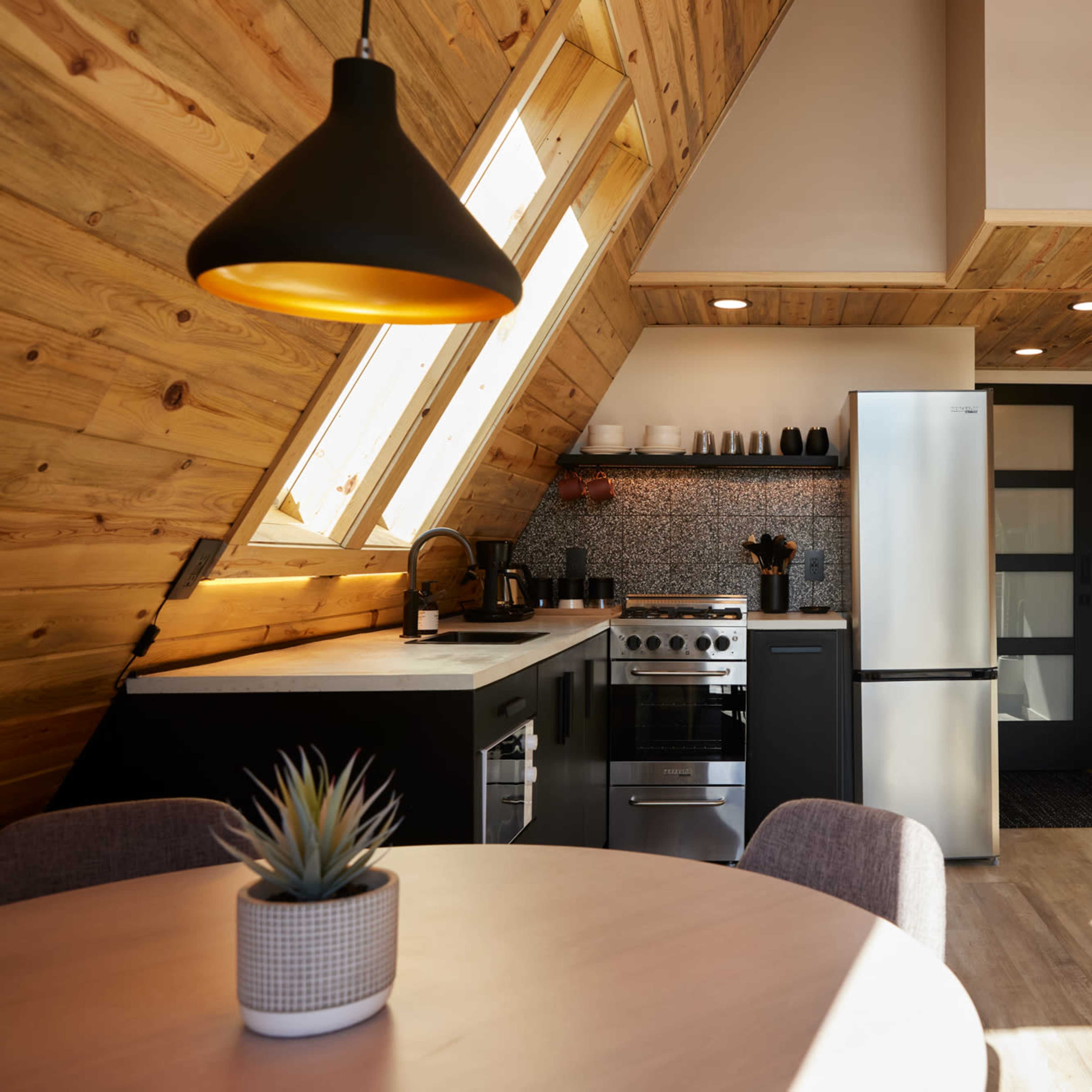 A modern kitchen with a triangular wooden ceiling features stainless steel appliances and a round dining table.