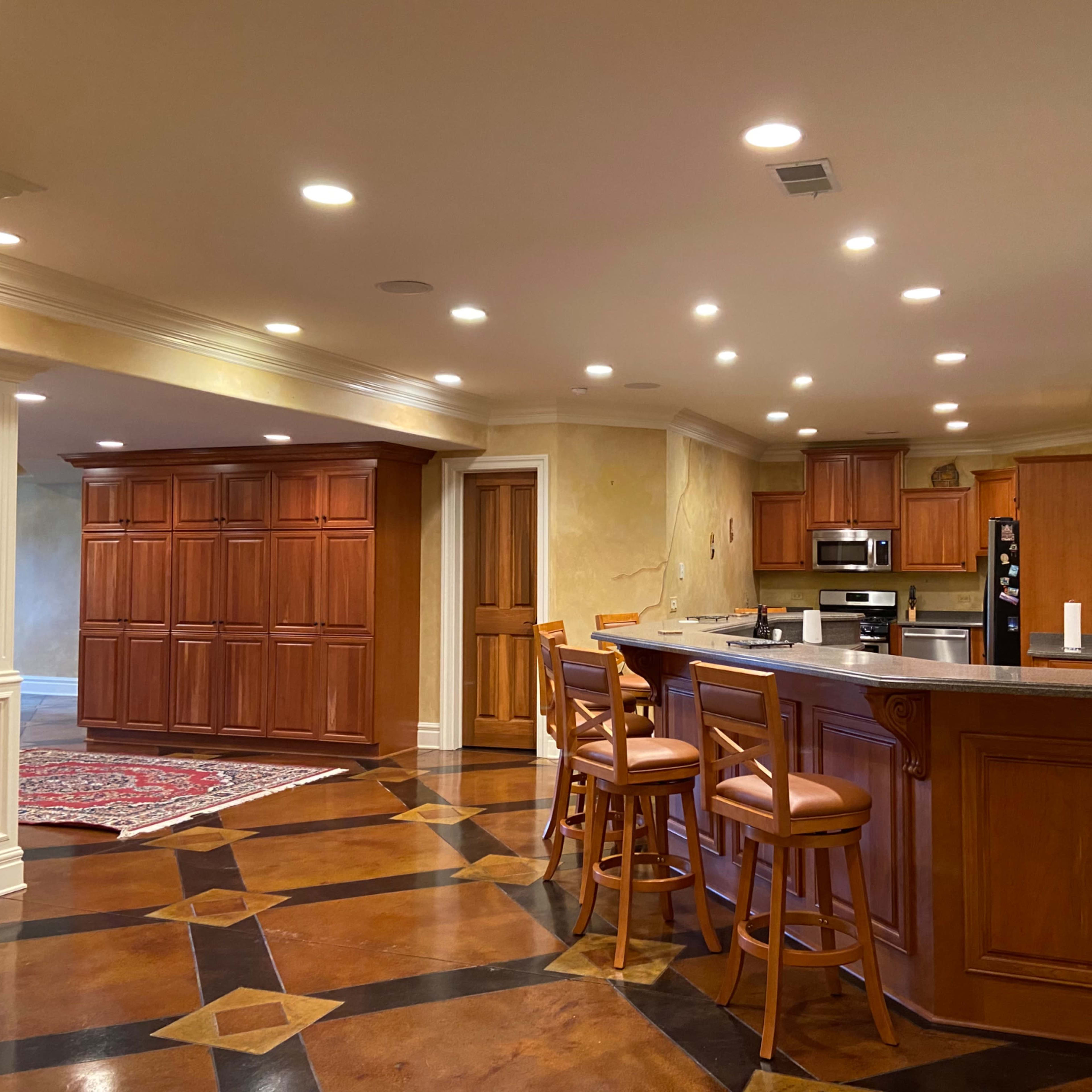 A spacious kitchen with wooden cabinets, a central island with bar seating, and a tiled floor featuring a geometric pattern.