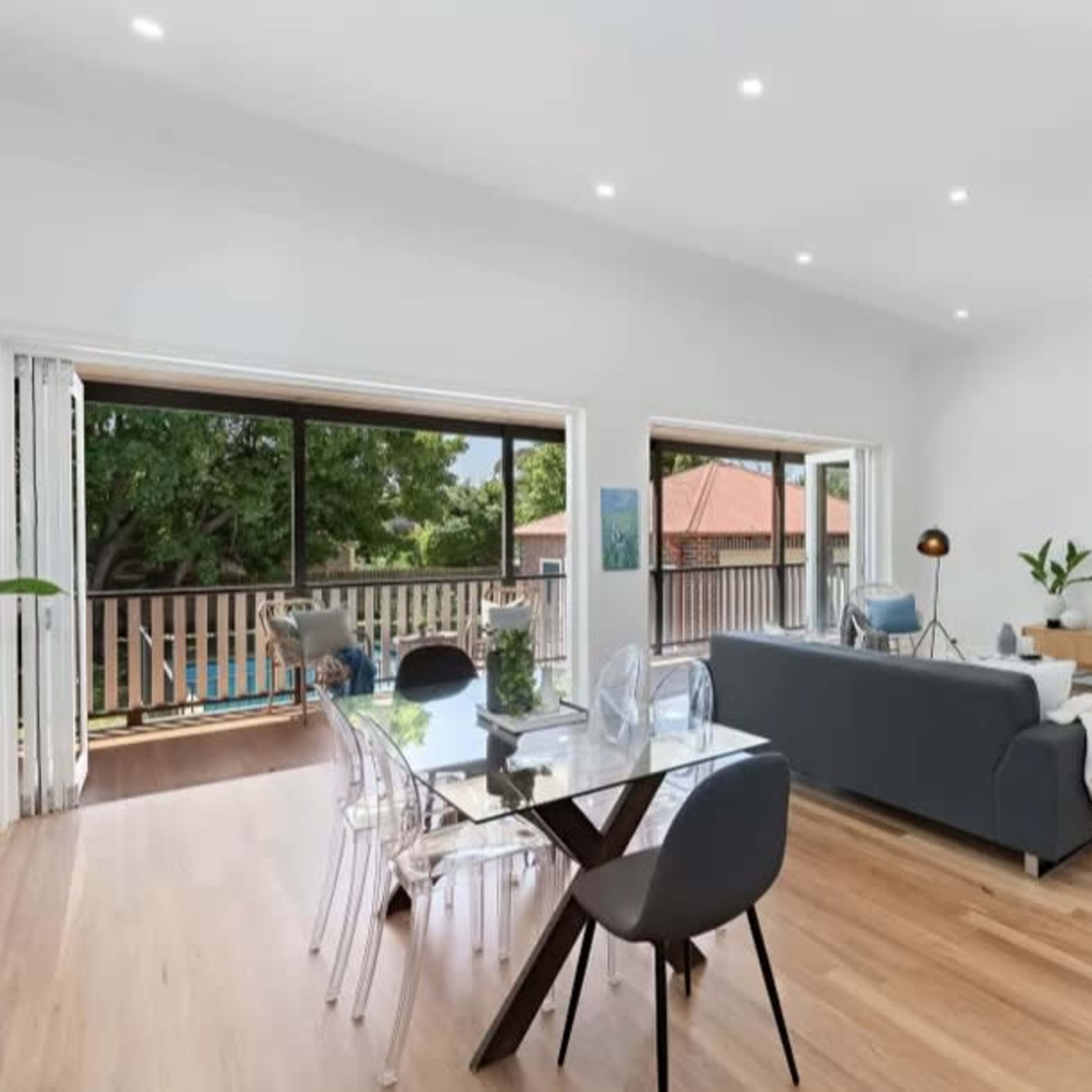 A modern living room and dining area with large windows, showcasing wooden floors and minimalist furniture.