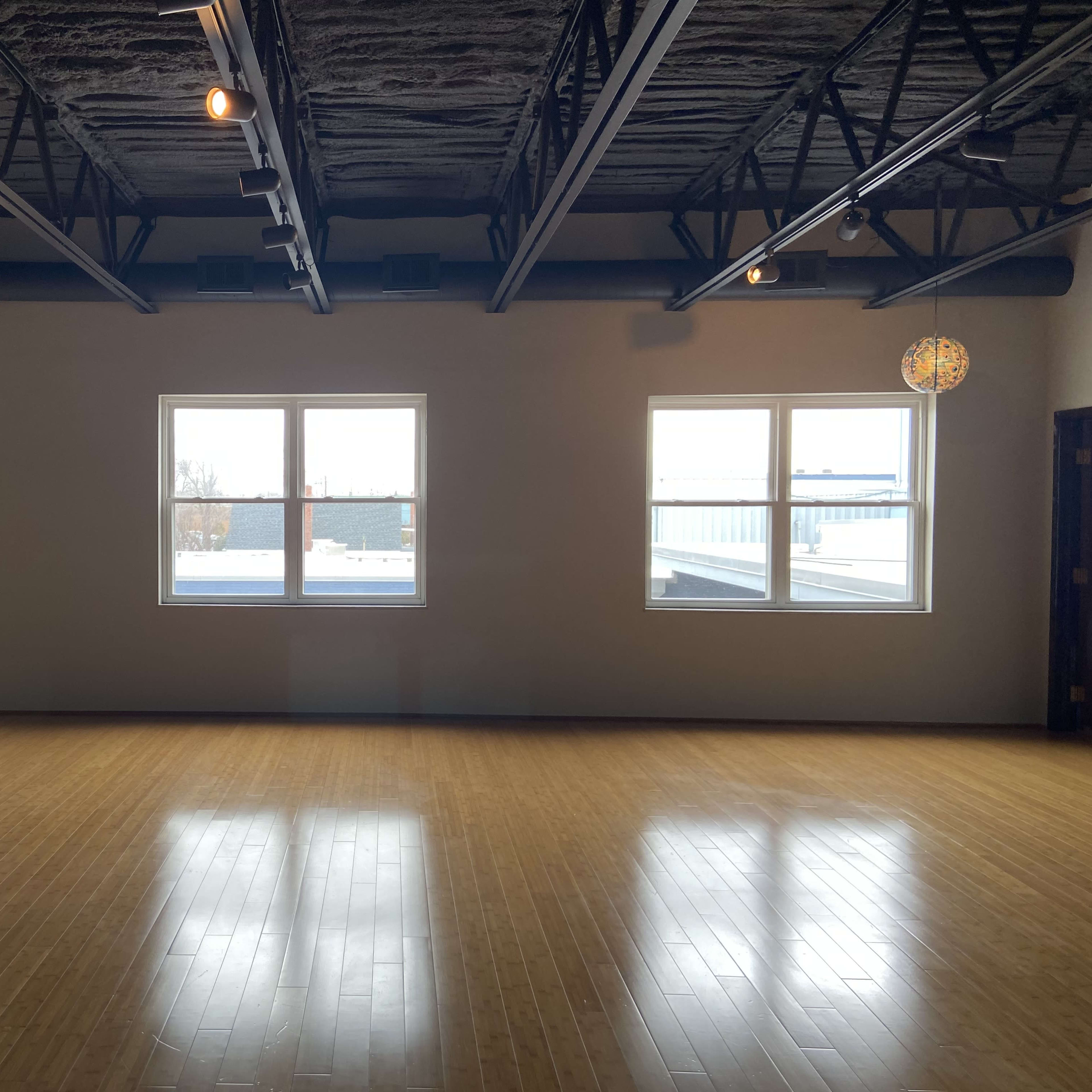 An empty room with a polished wooden floor, large windows, and decorative hanging lights.