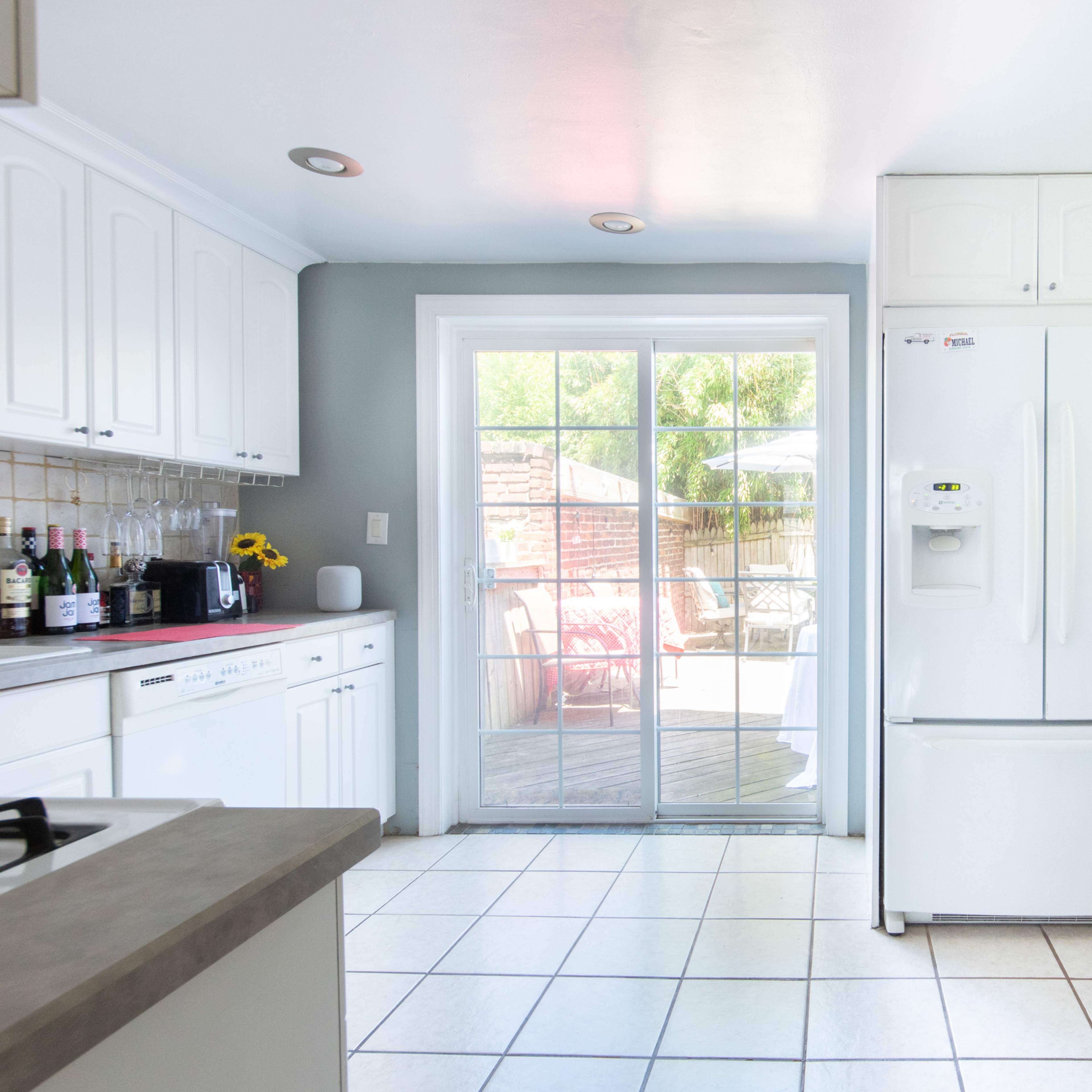 A kitchen features a white refrigerator, light-colored cabinets, and a sliding glass door leading to an outdoor deck.