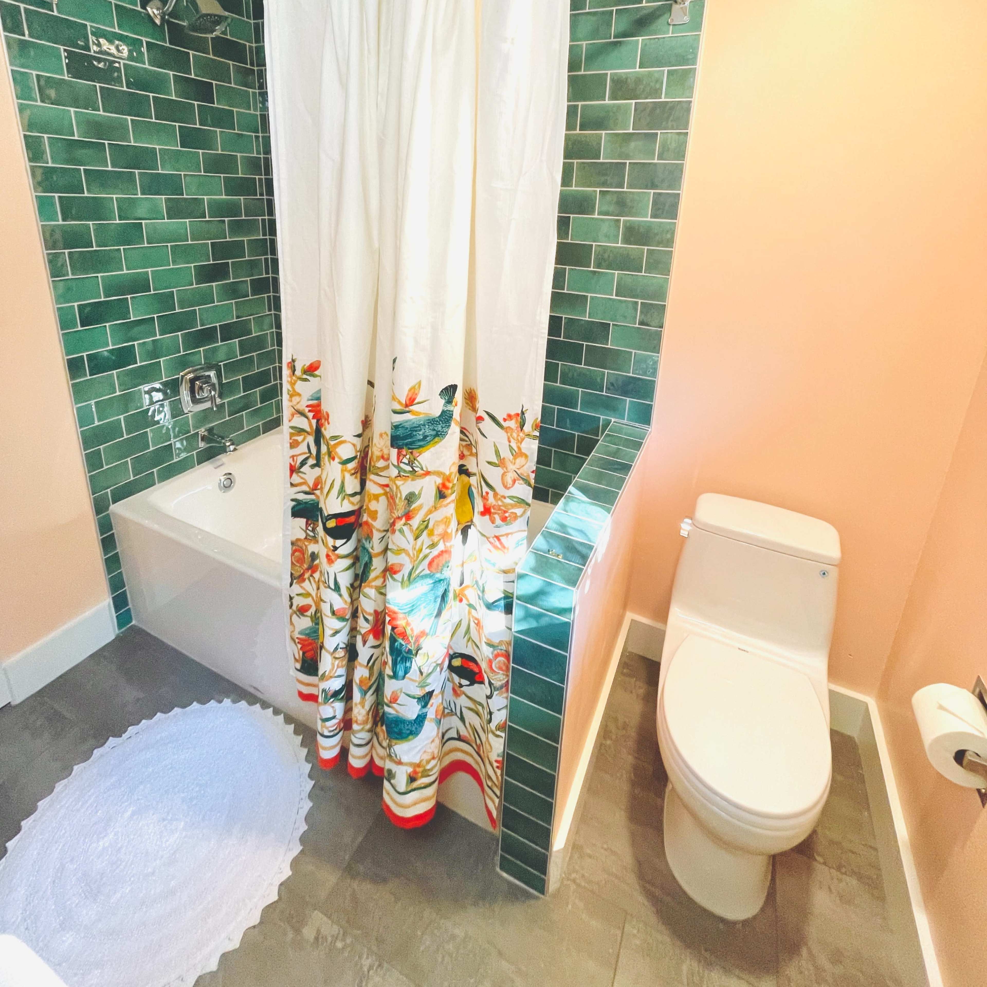 A bathroom with a bathtub, a colorful shower curtain, green tiled walls, and a white toilet.