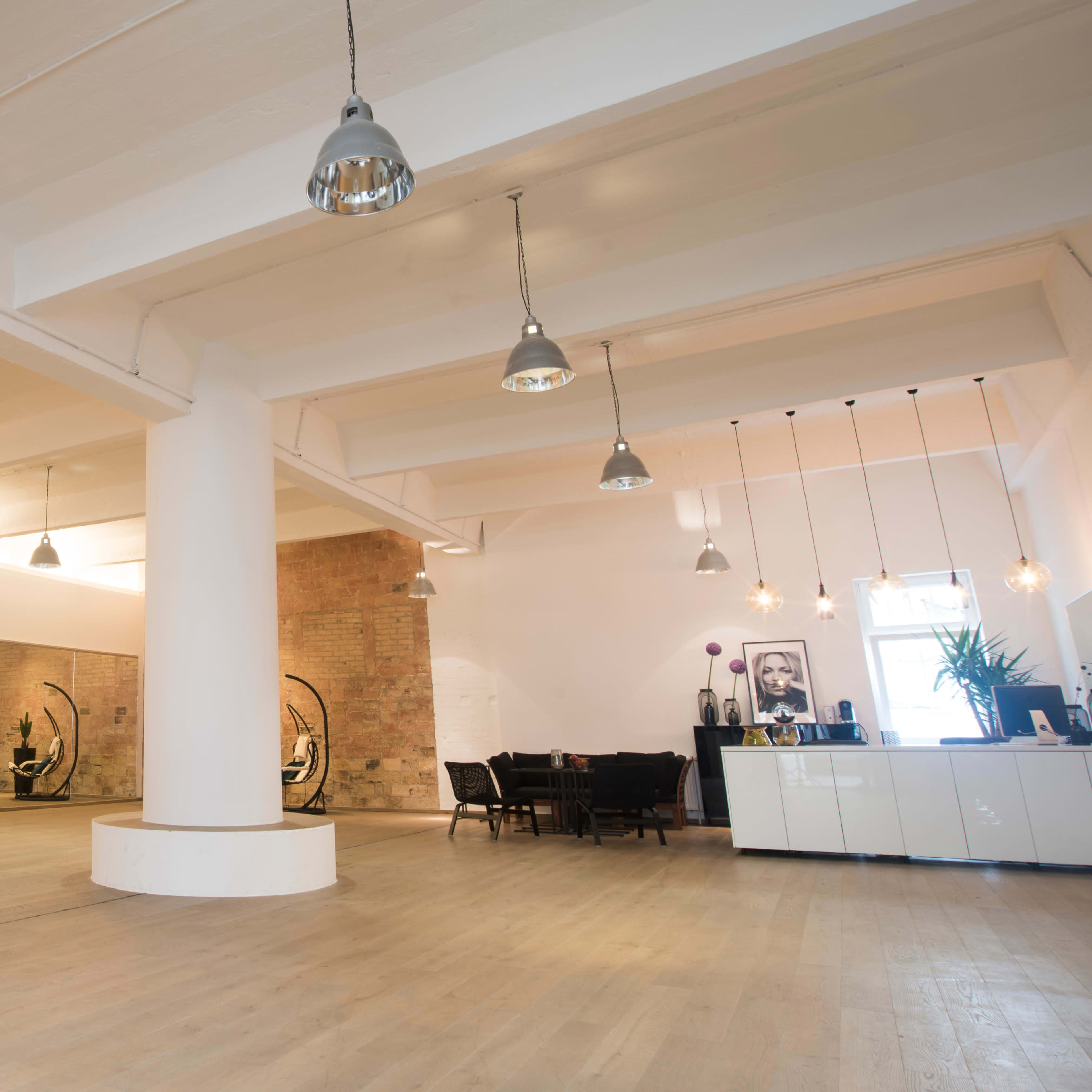 An interior space featuring a large, open room with hardwood flooring, high ceilings, and a mix of modern and industrial design elements, including hanging lights and a mirrored wall.