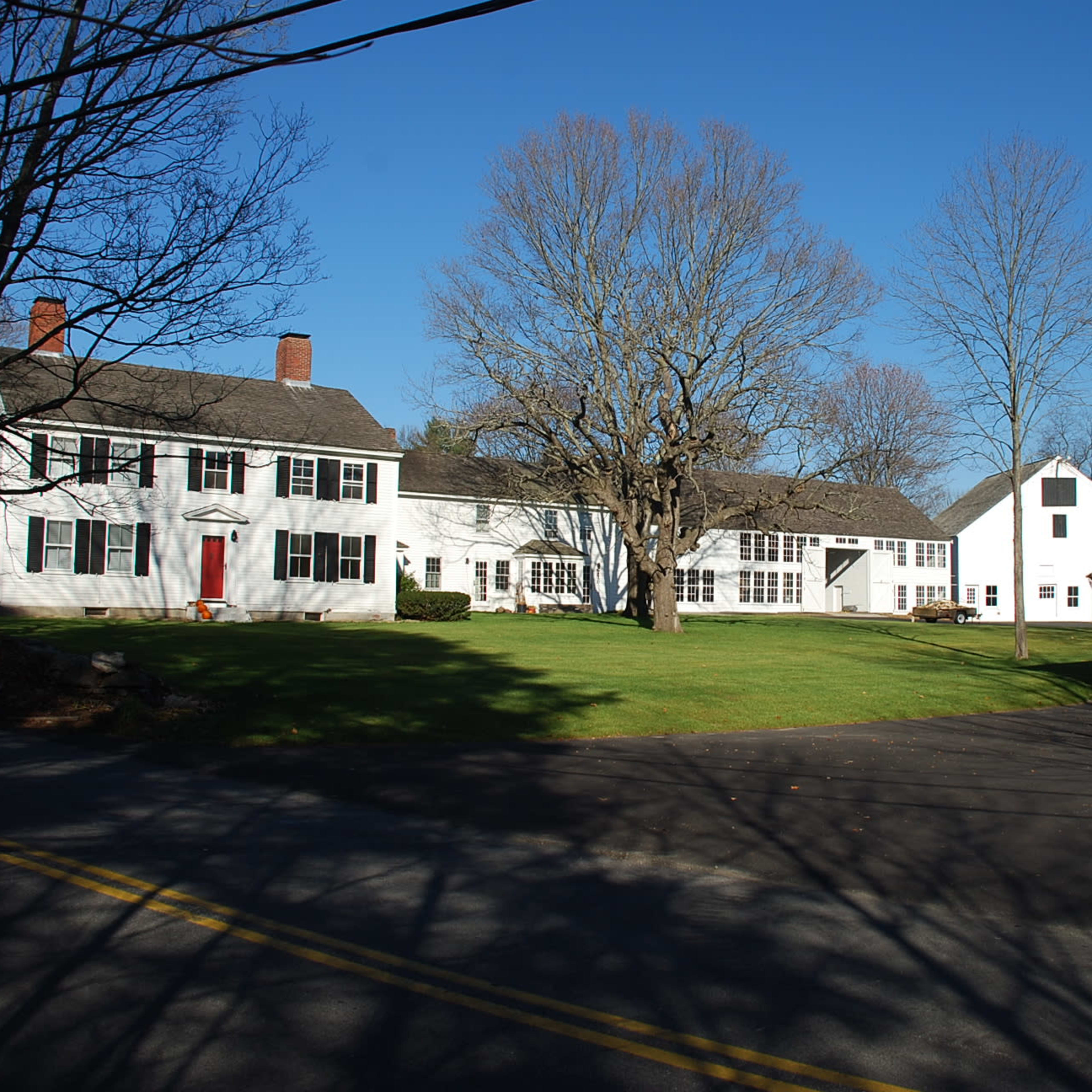 A large white house complex with multiple buildings, a well-maintained lawn, and a stone structure at the roadside.