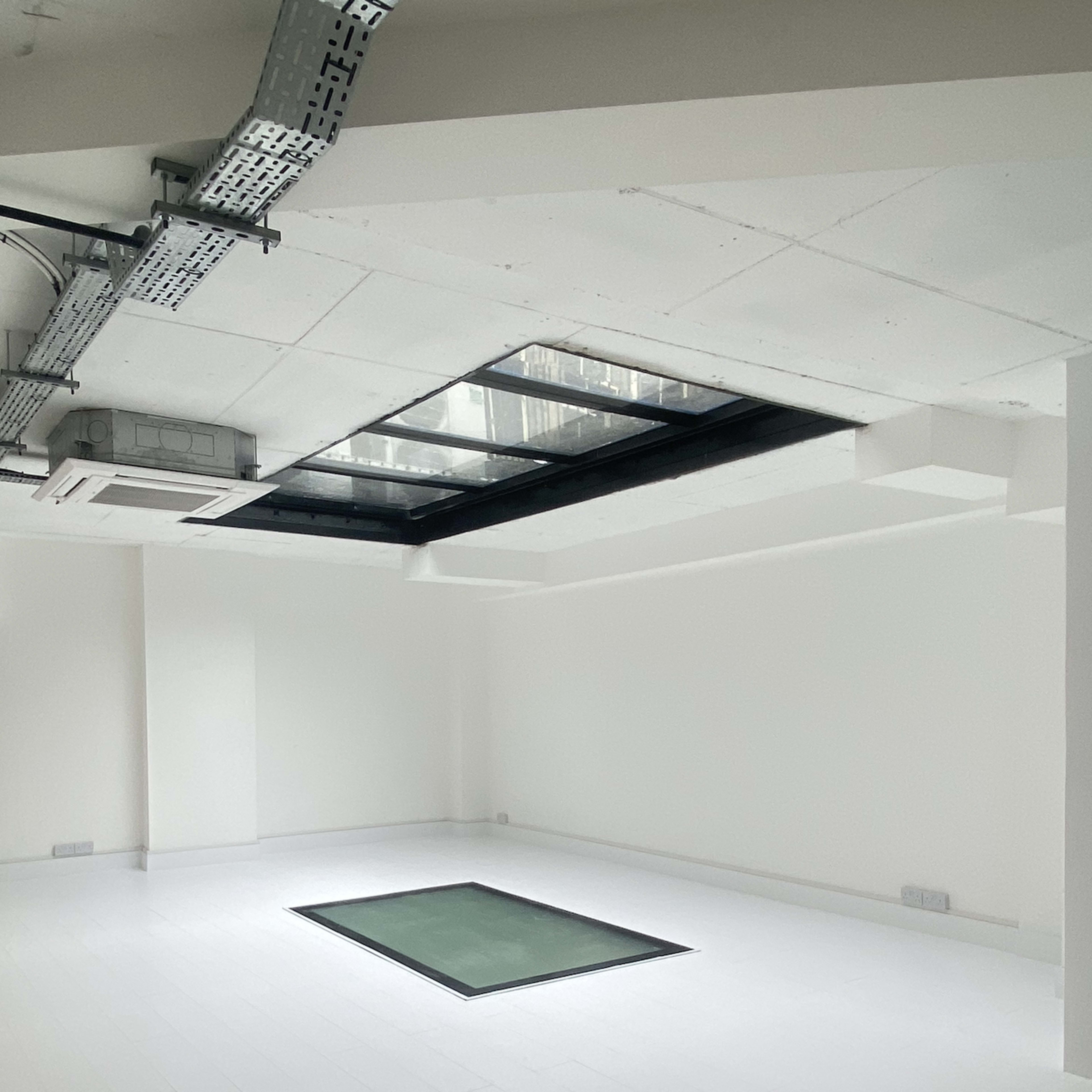 A sparsely furnished room with white walls and flooring, featuring a rectangular glass section in the center of the floor.