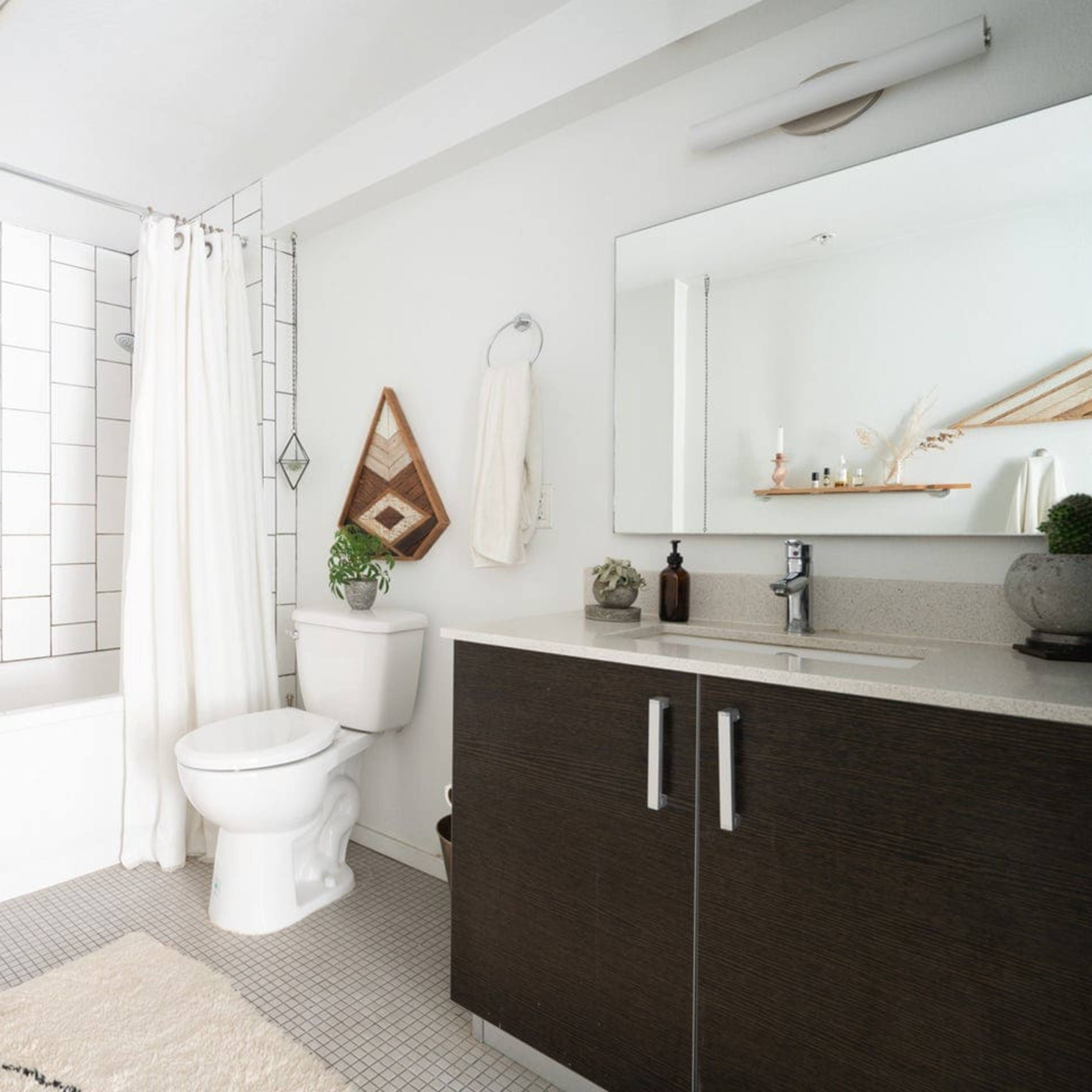 A modern bathroom featuring a bathtub, a white shower curtain, a toilet, and a sink with dark cabinetry.