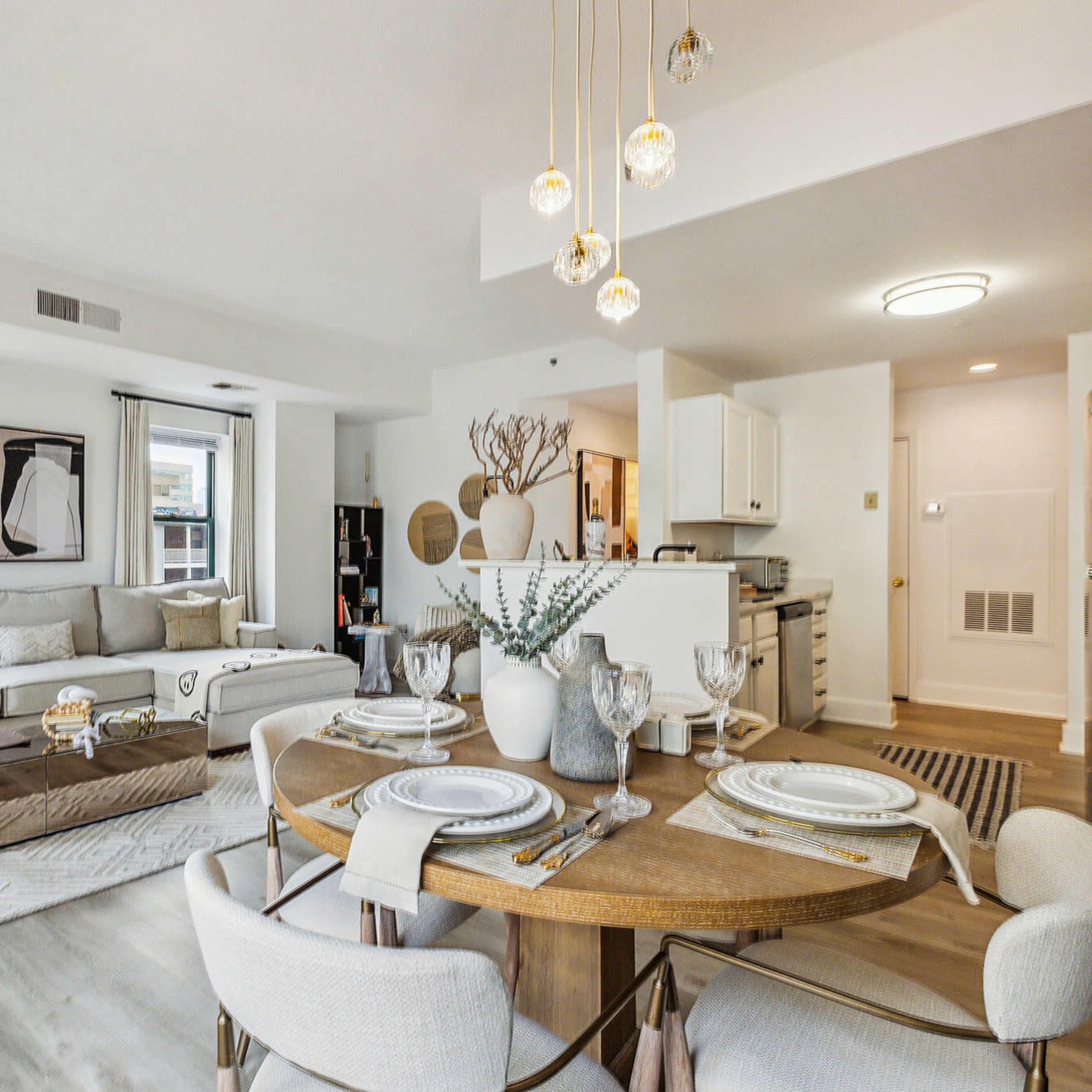 A modern living space featuring a beige sectional sofa, a round dining table set for four, and an open kitchen area with white cabinetry.