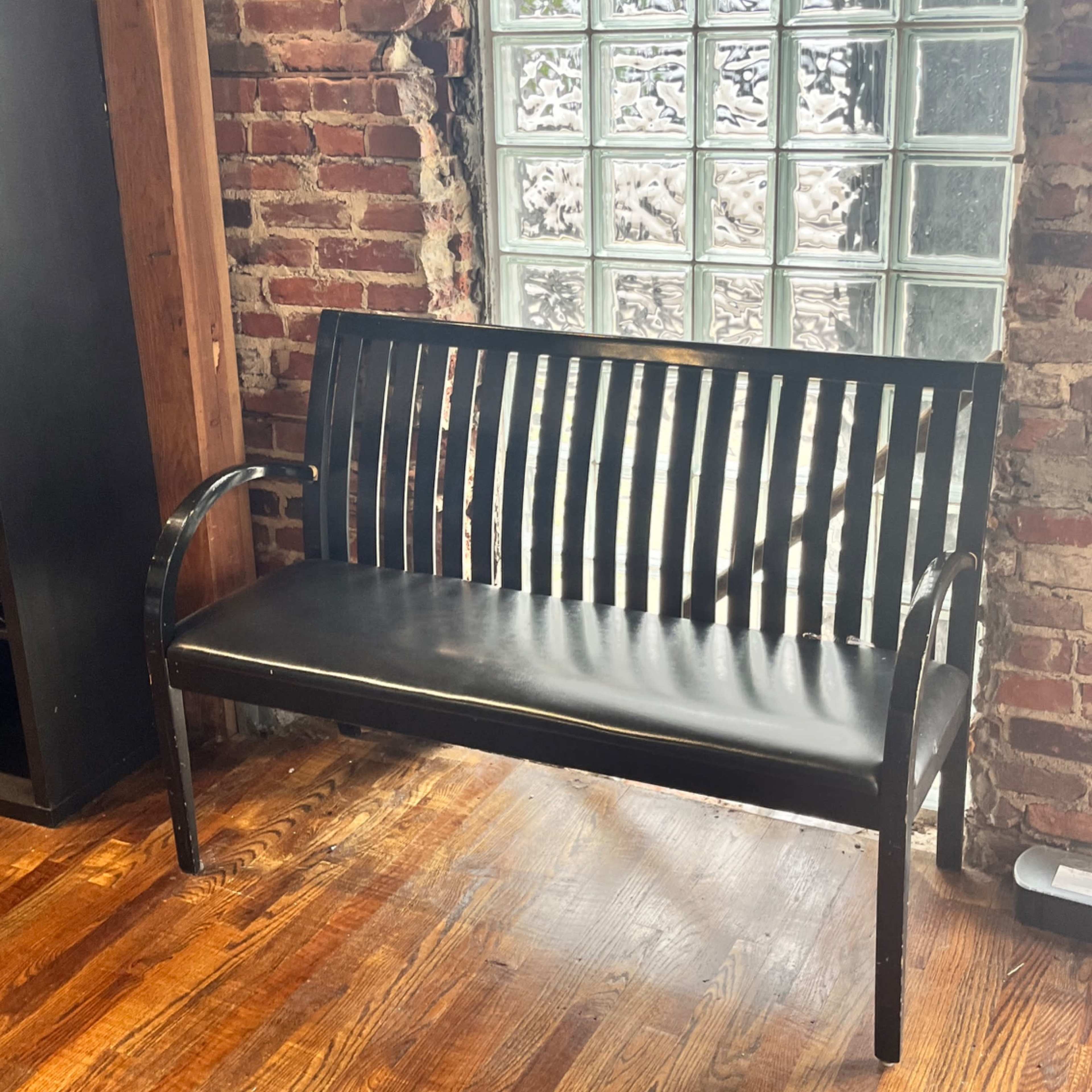 A black metal bench placed against a brick wall with a glass block window beside it.